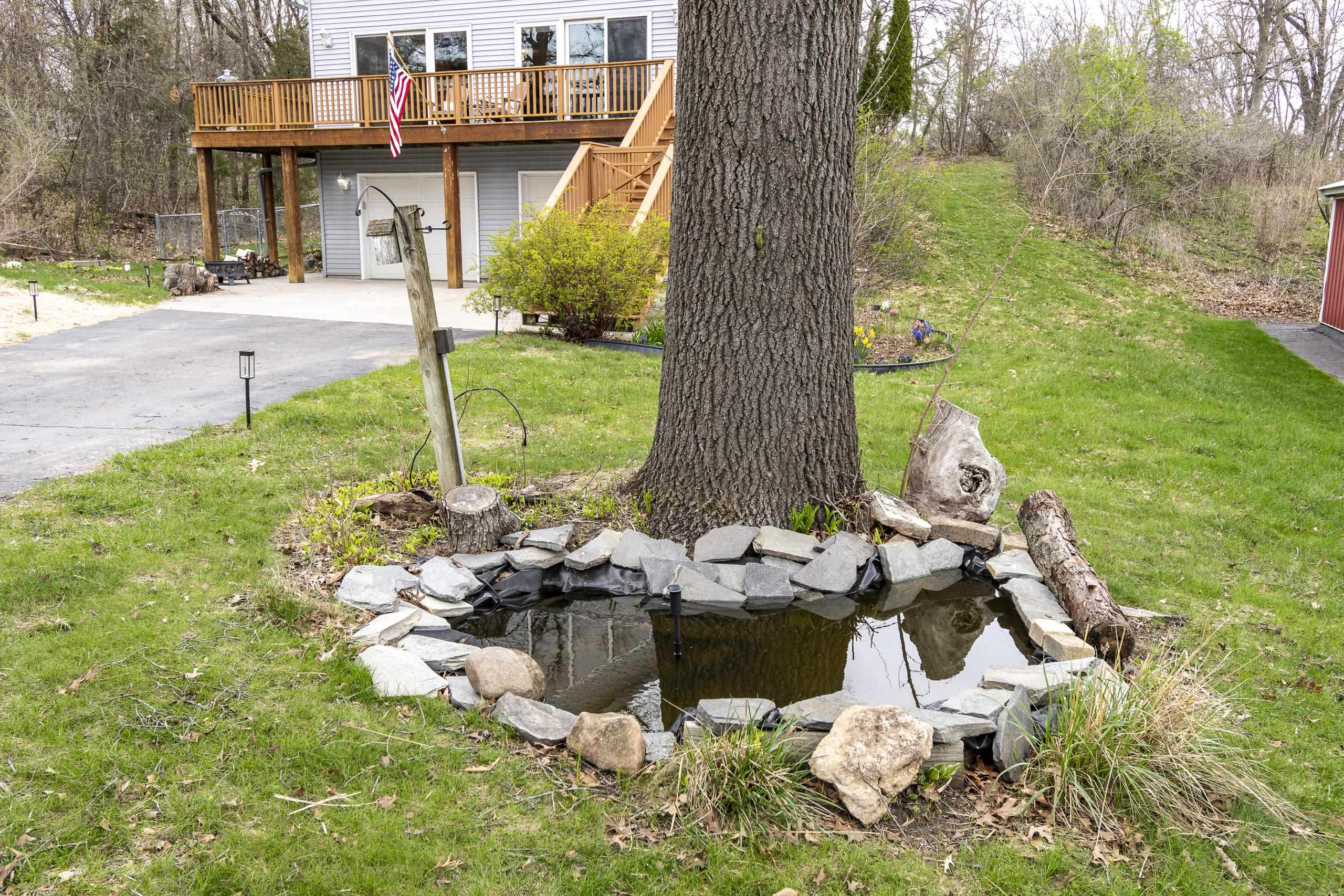 Landscaped yard with a stone-edged pond around a large tree and a raised wooden deck.