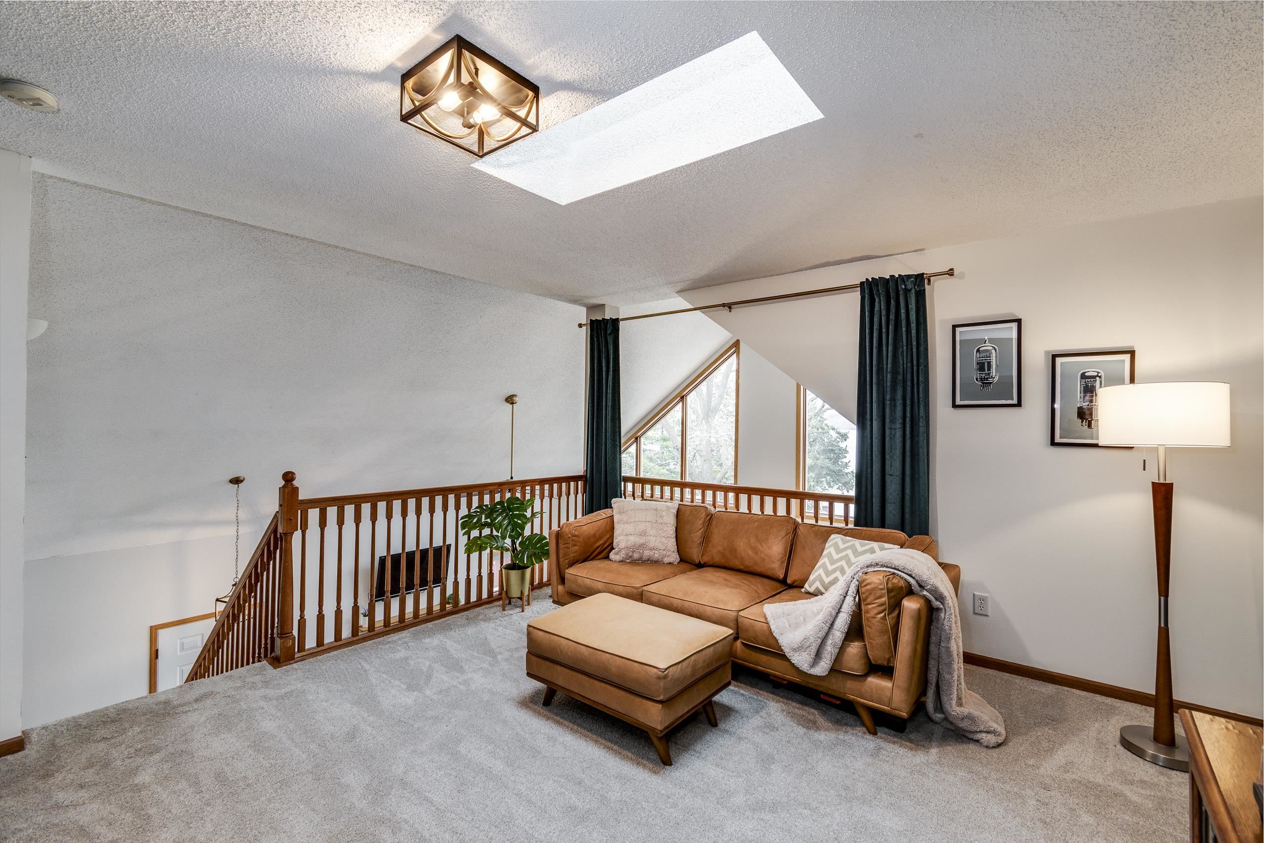 Upper-level living room with a leather sectional, skylight, and tall angular windows.