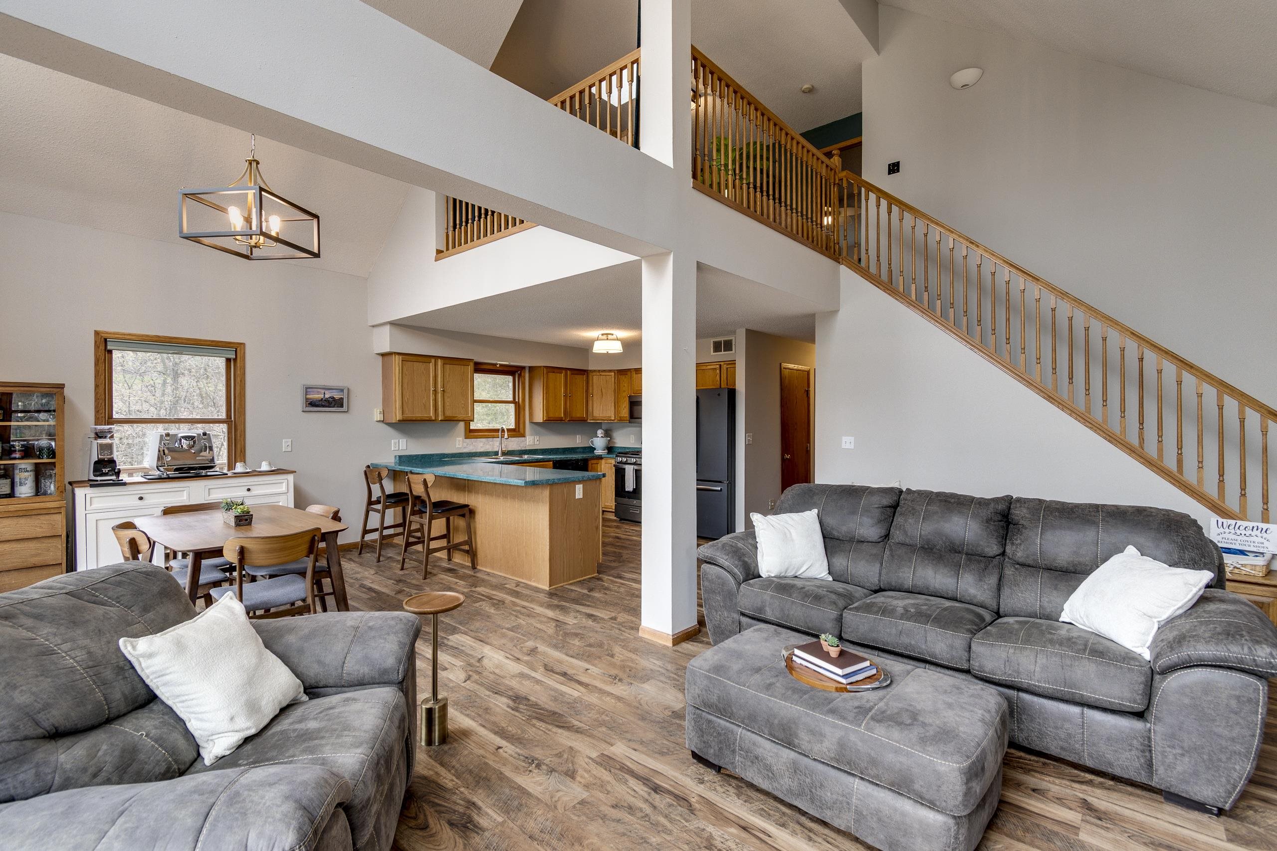 Open-concept living room with gray sofas, a kitchen island, and a wooden staircase to the loft.