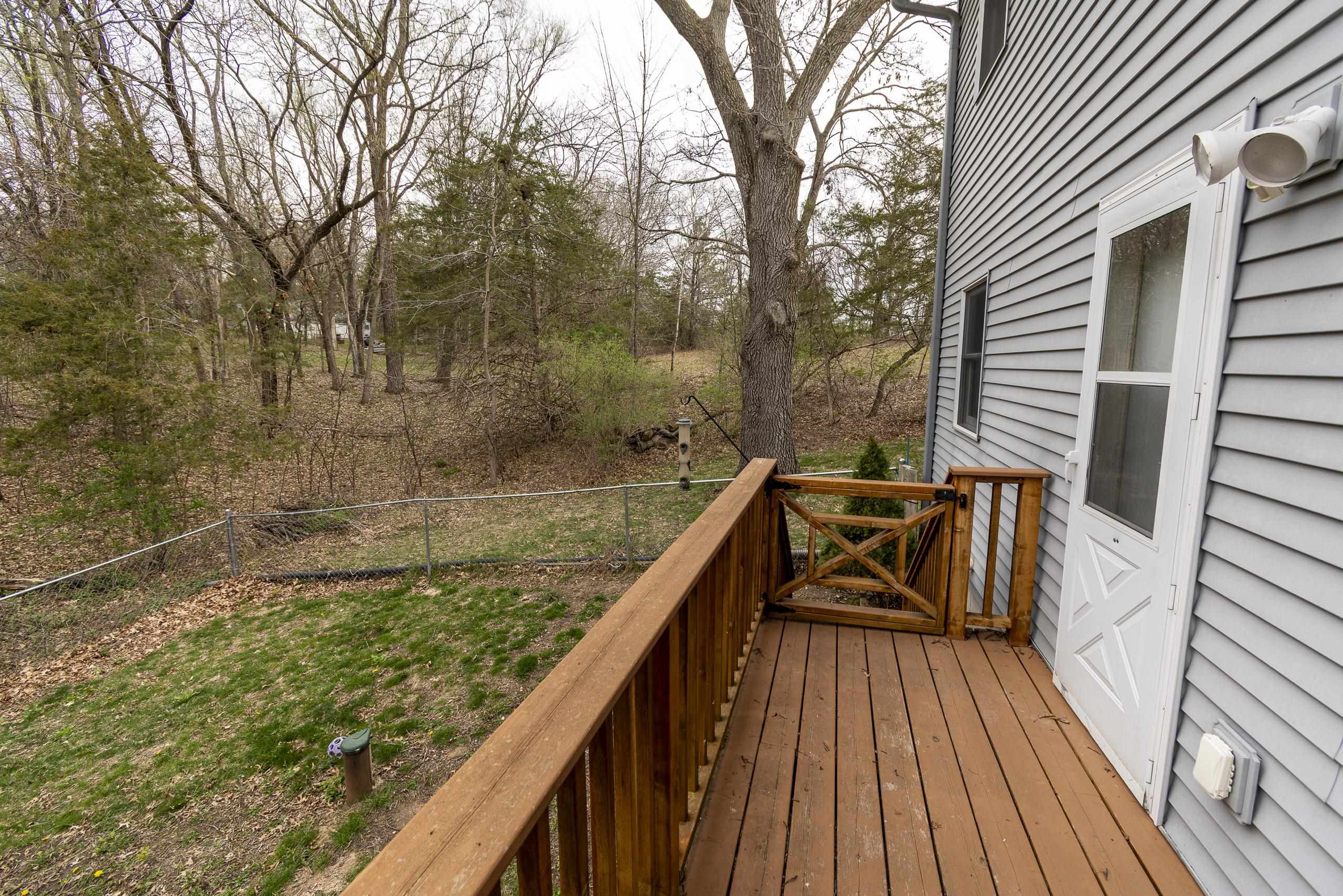 Wooden rear deck overlooking a fenced, leaf-covered wooded yard beside gray siding.