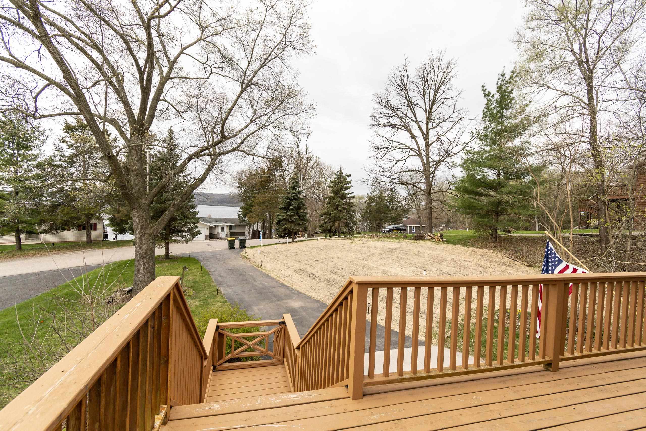 Wooden deck overlooks a bare yard, neighboring homes, and a lake beyond the road.