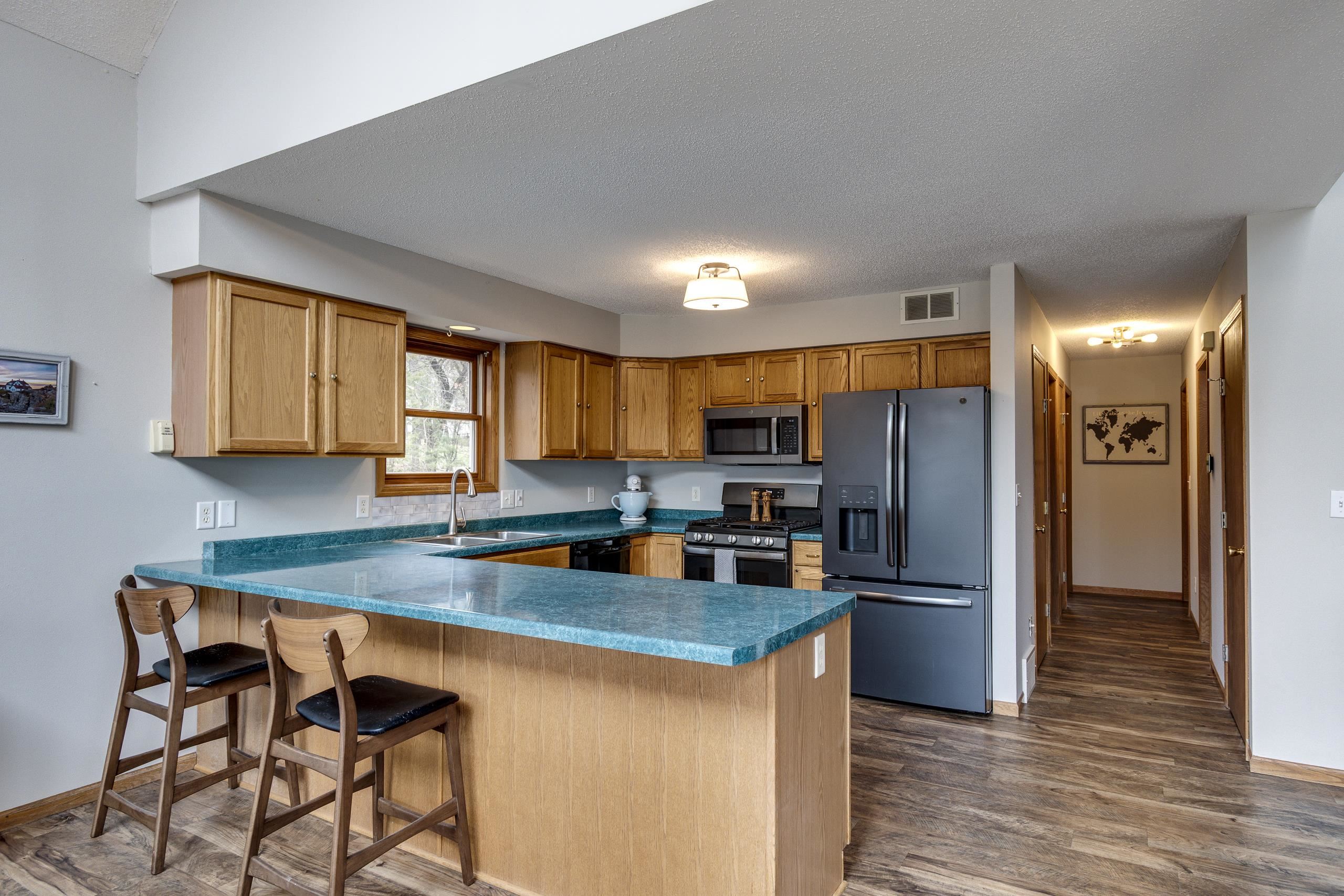 Kitchen with turquoise island countertop, wood cabinets, stainless steel appliances, and two bar stools.
