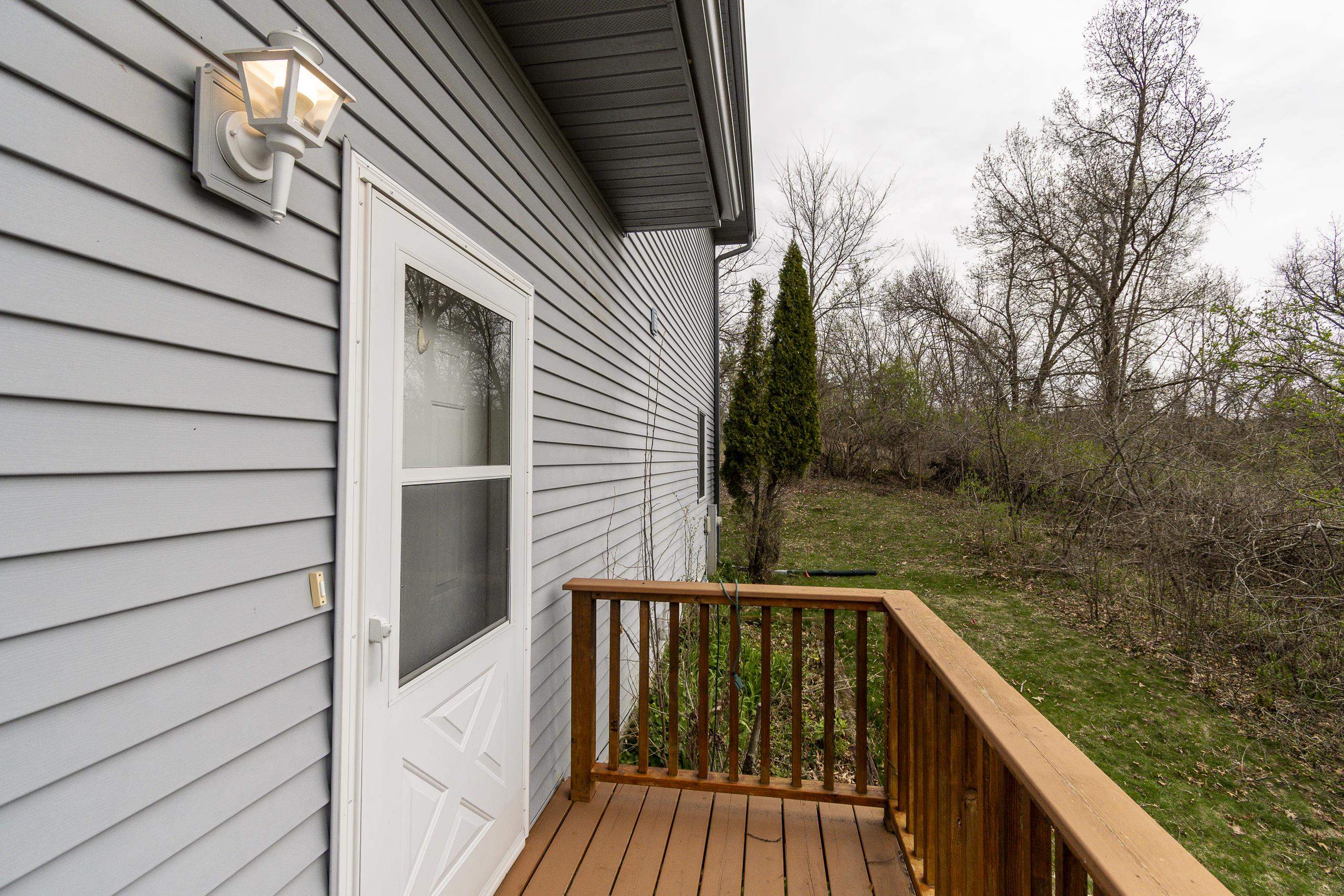Wooden deck beside a gray-sided house, overlooking a grassy backyard bordered by leafless trees.