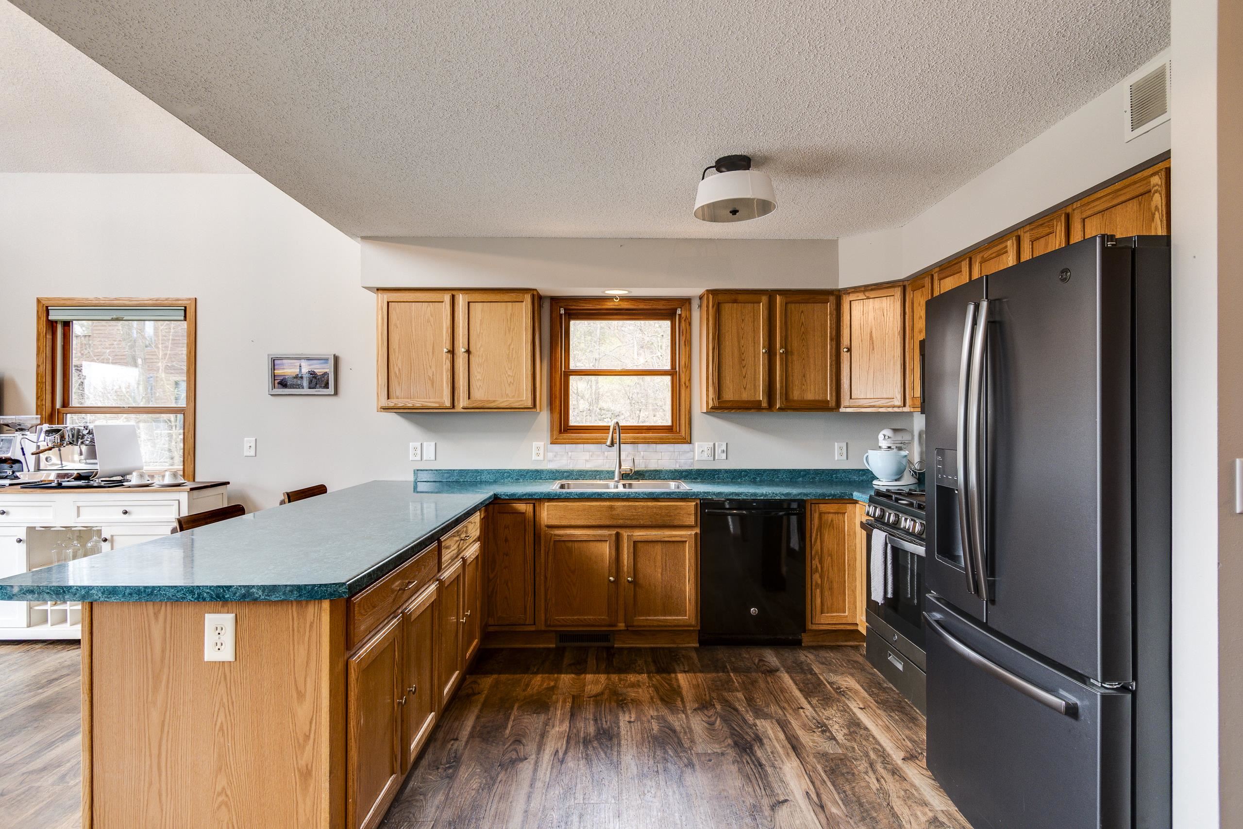 Kitchen with warm wood cabinets, turquoise countertops, a large peninsula, and dark appliances.