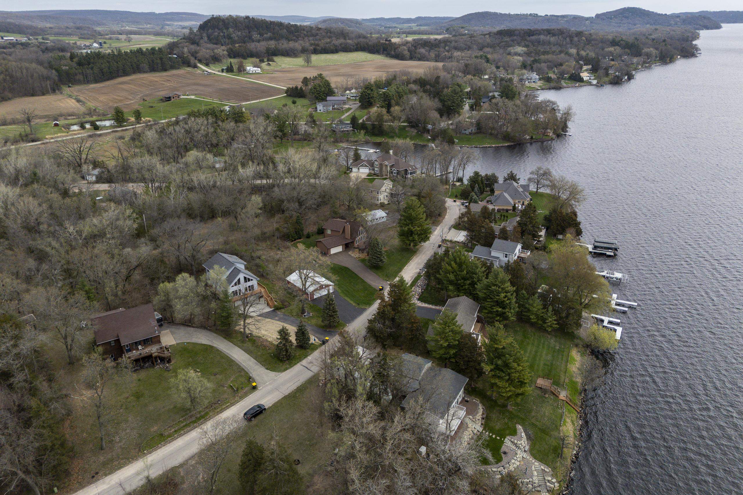 Aerial view of lakeside homes among trees, with docks along the shore and farmland beyond.