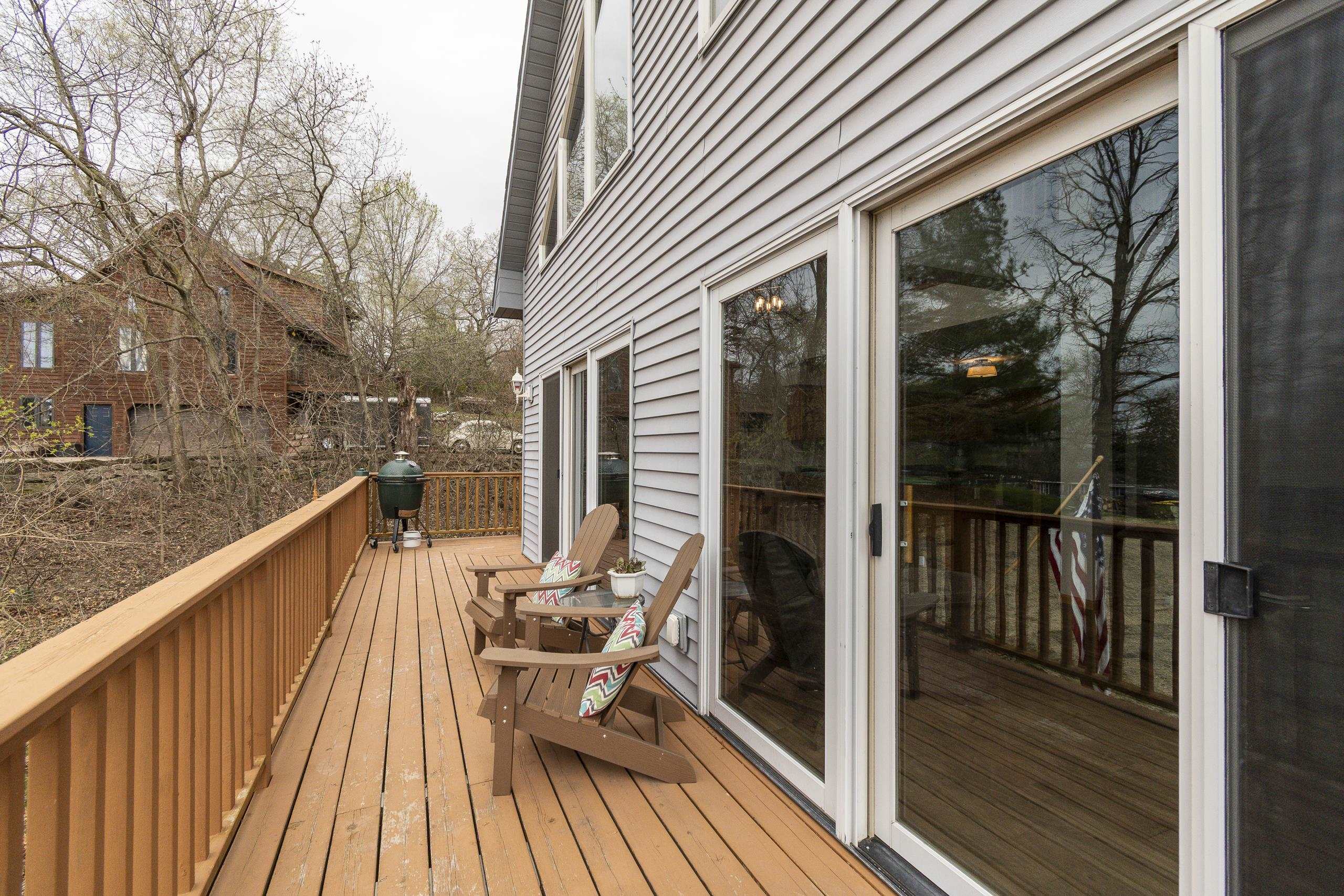 Wooden deck with Adirondack chairs and grill beside large sliding glass doors.