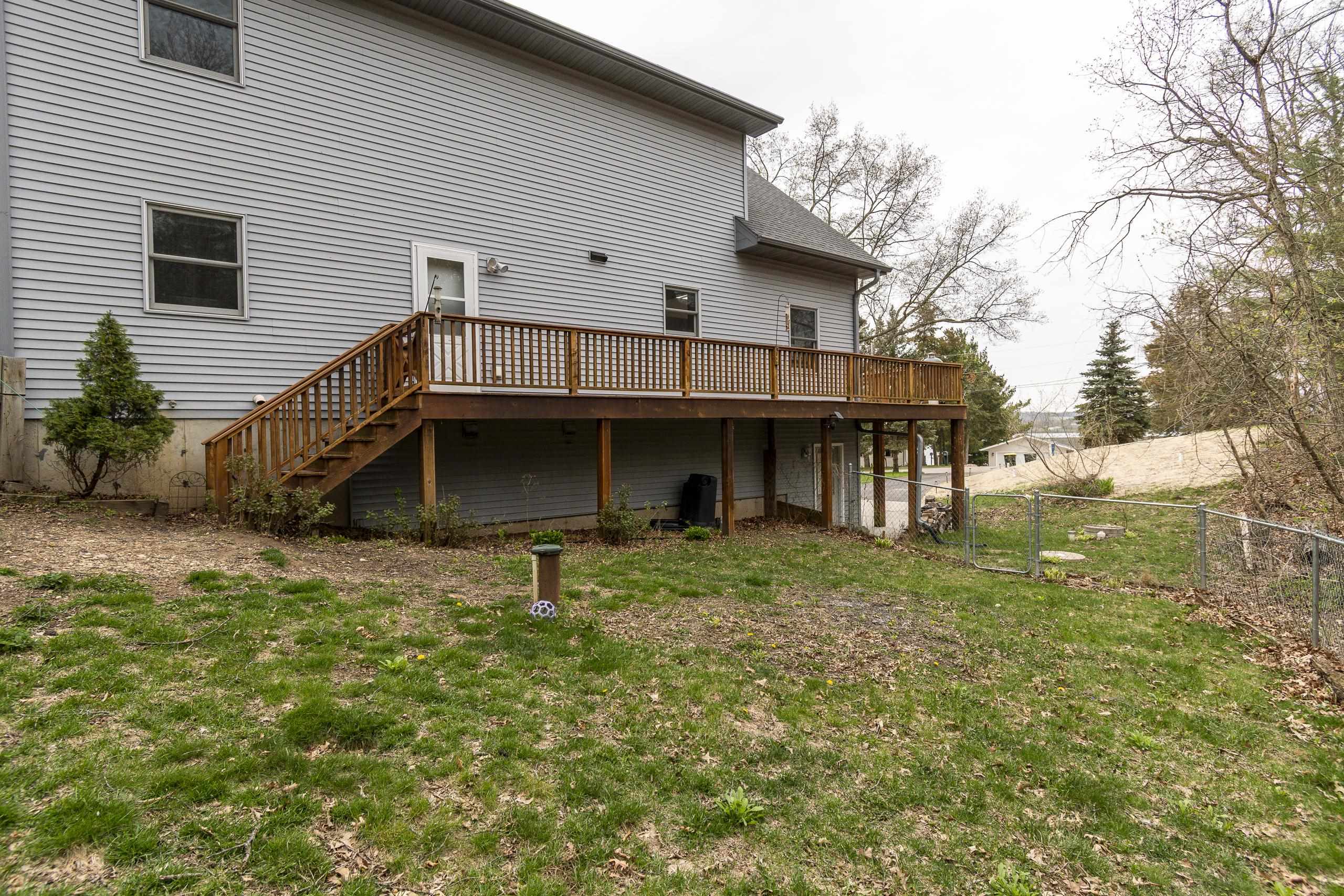 Gray-sided house with a raised wooden deck and stairs overlooking a fenced yard.