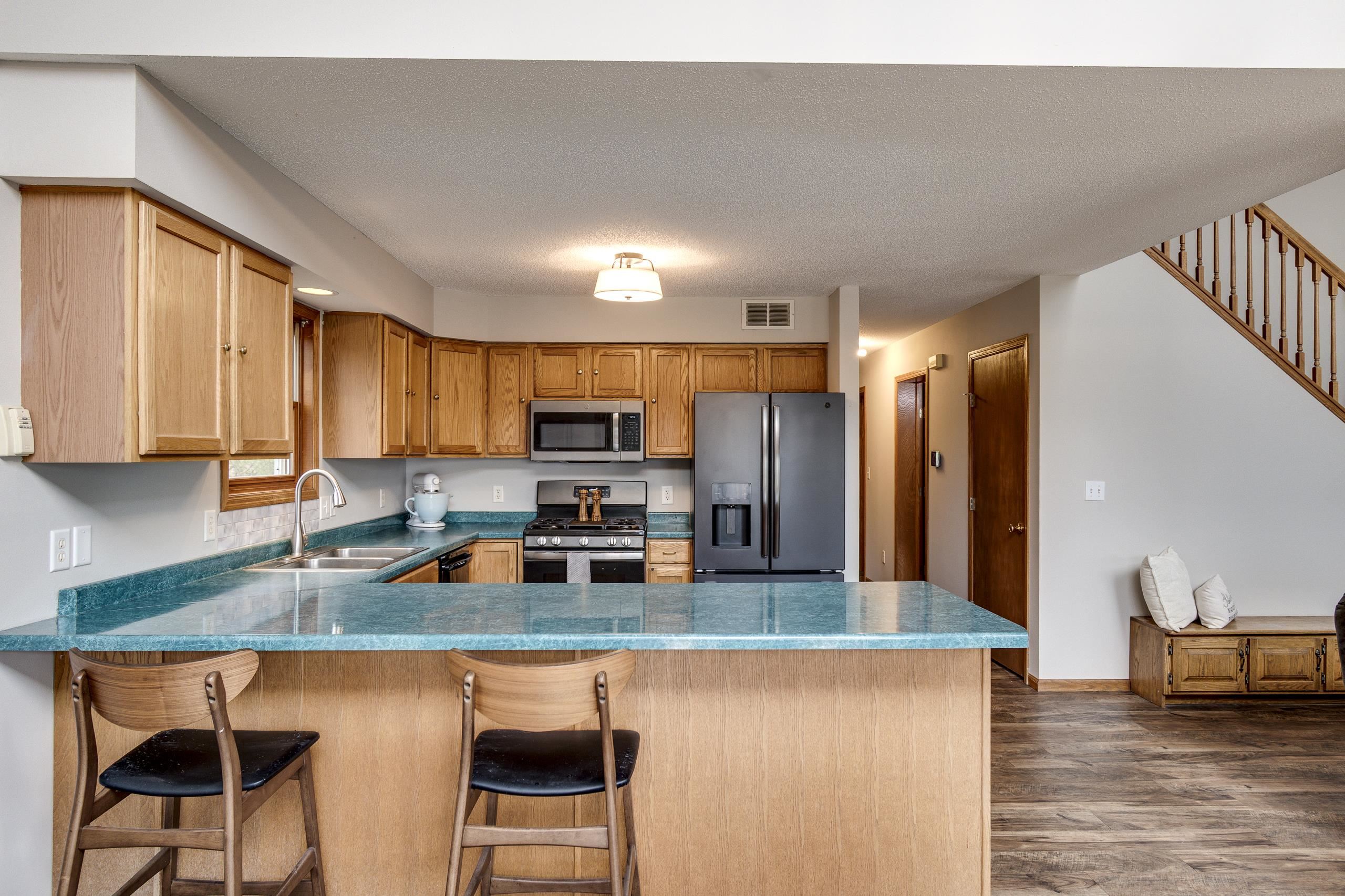 Kitchen with a turquoise island, wood cabinets, stainless-steel appliances, and a staircase.