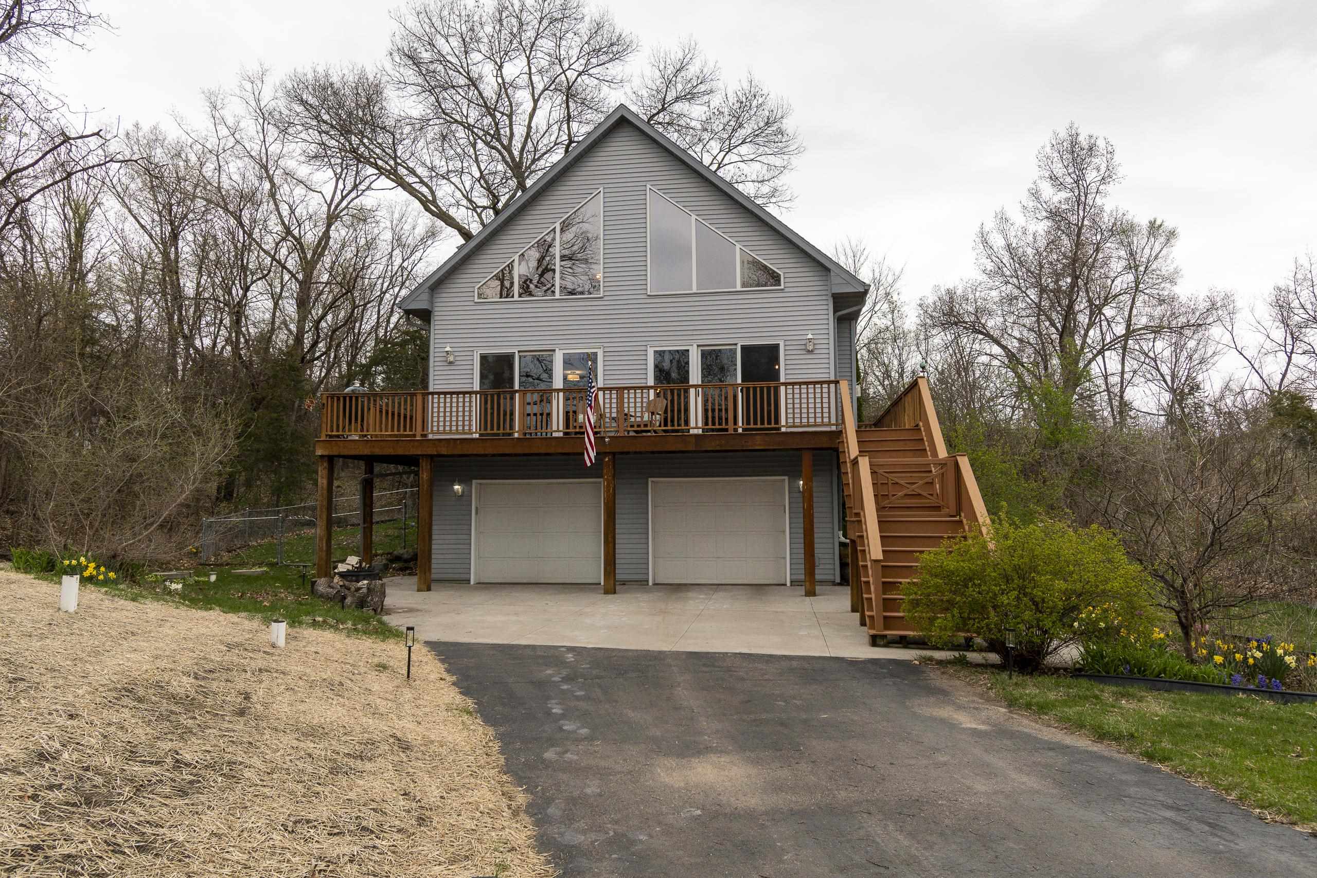 Gray gabled home with a raised wooden deck, exterior stairs, and two garage doors beneath it.