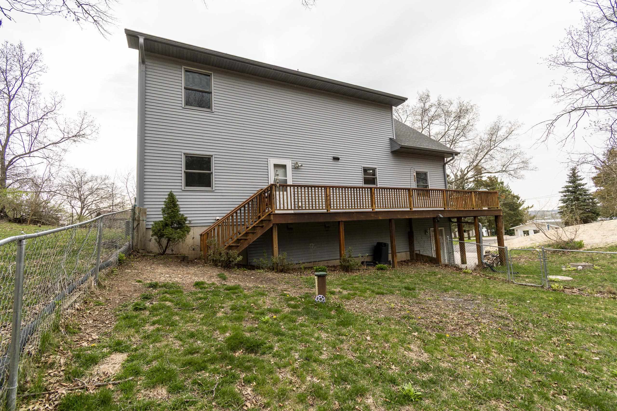 Gray-sided house with a raised wooden deck and fenced yard viewed from behind.