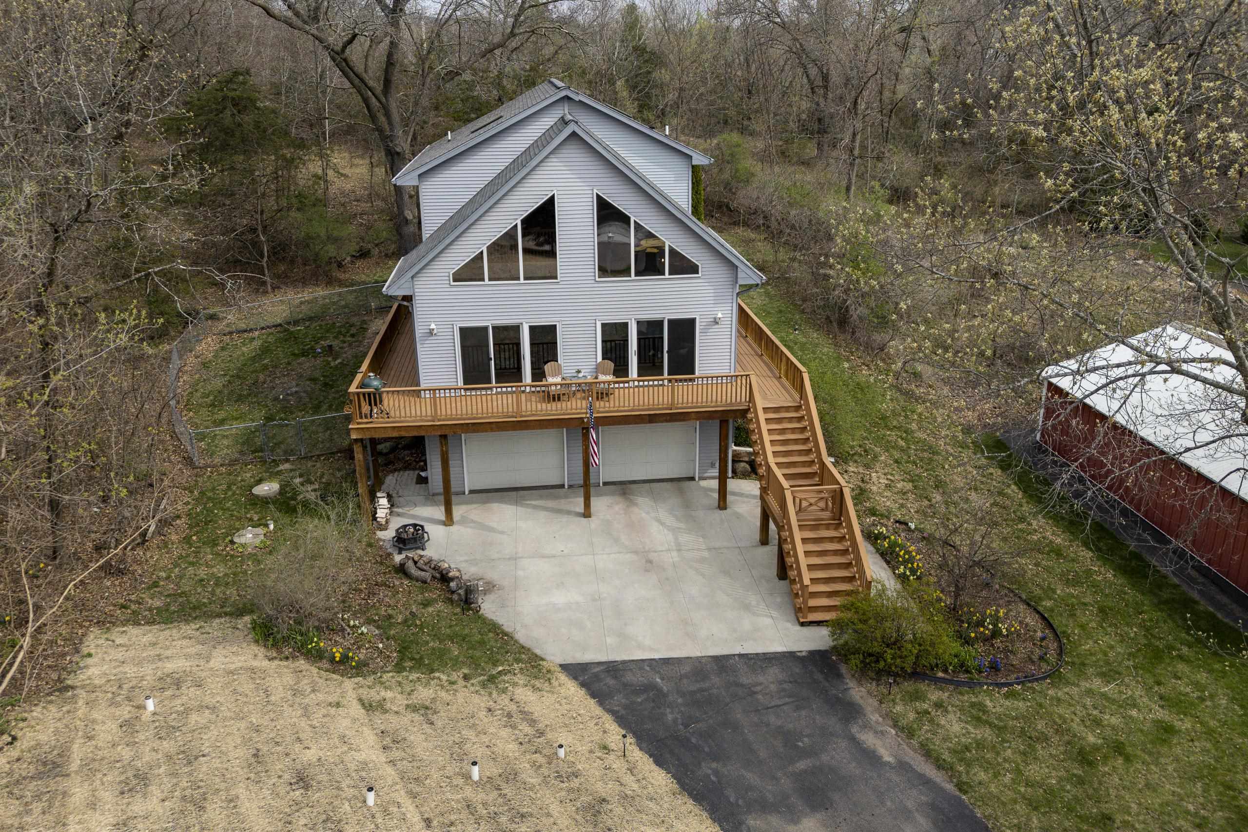 Gray-sided home with a raised wooden deck, exterior staircase, and two-car garage, seen from above.