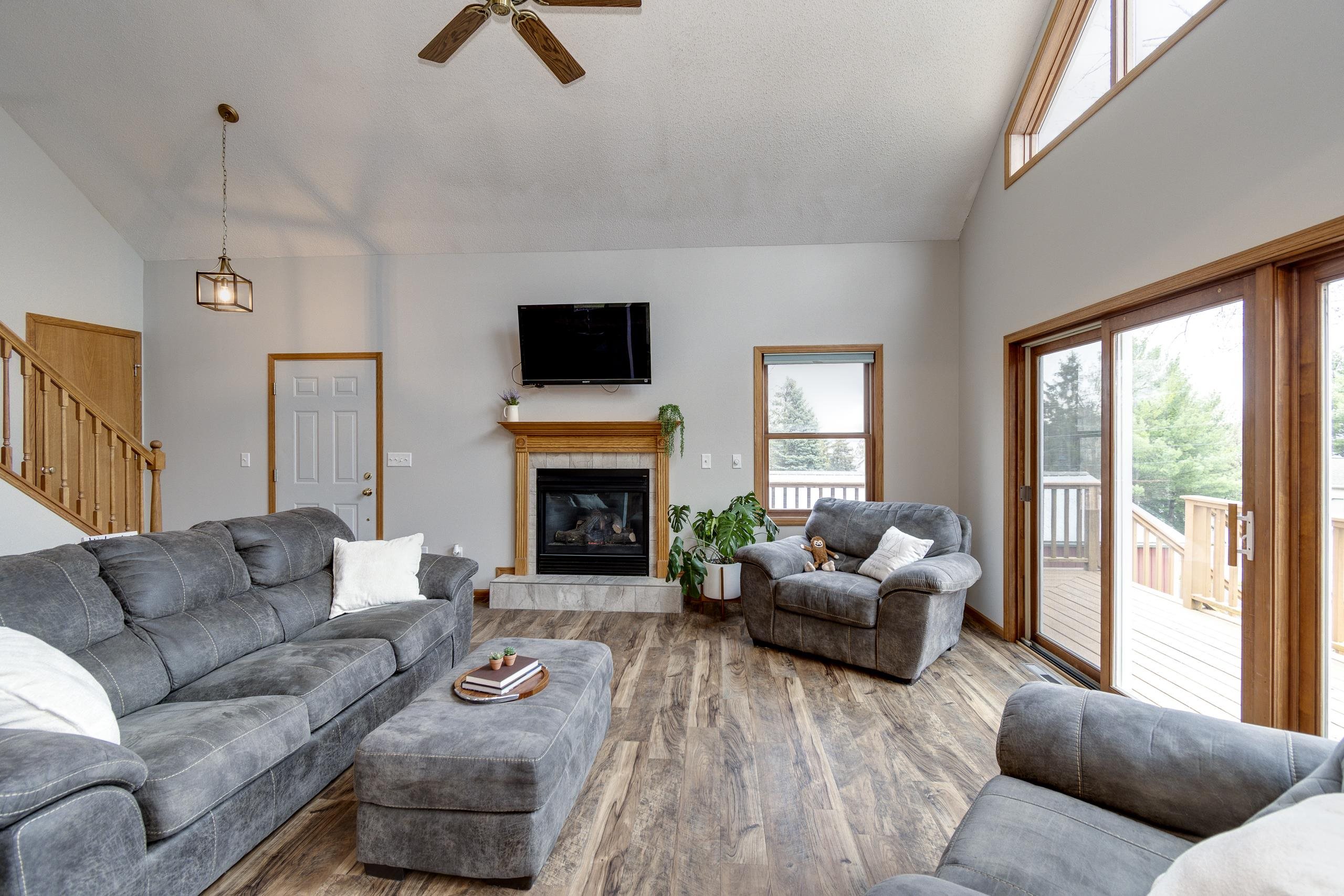 Living room with a fireplace, gray seating, vaulted ceiling, and sliding doors to a deck.