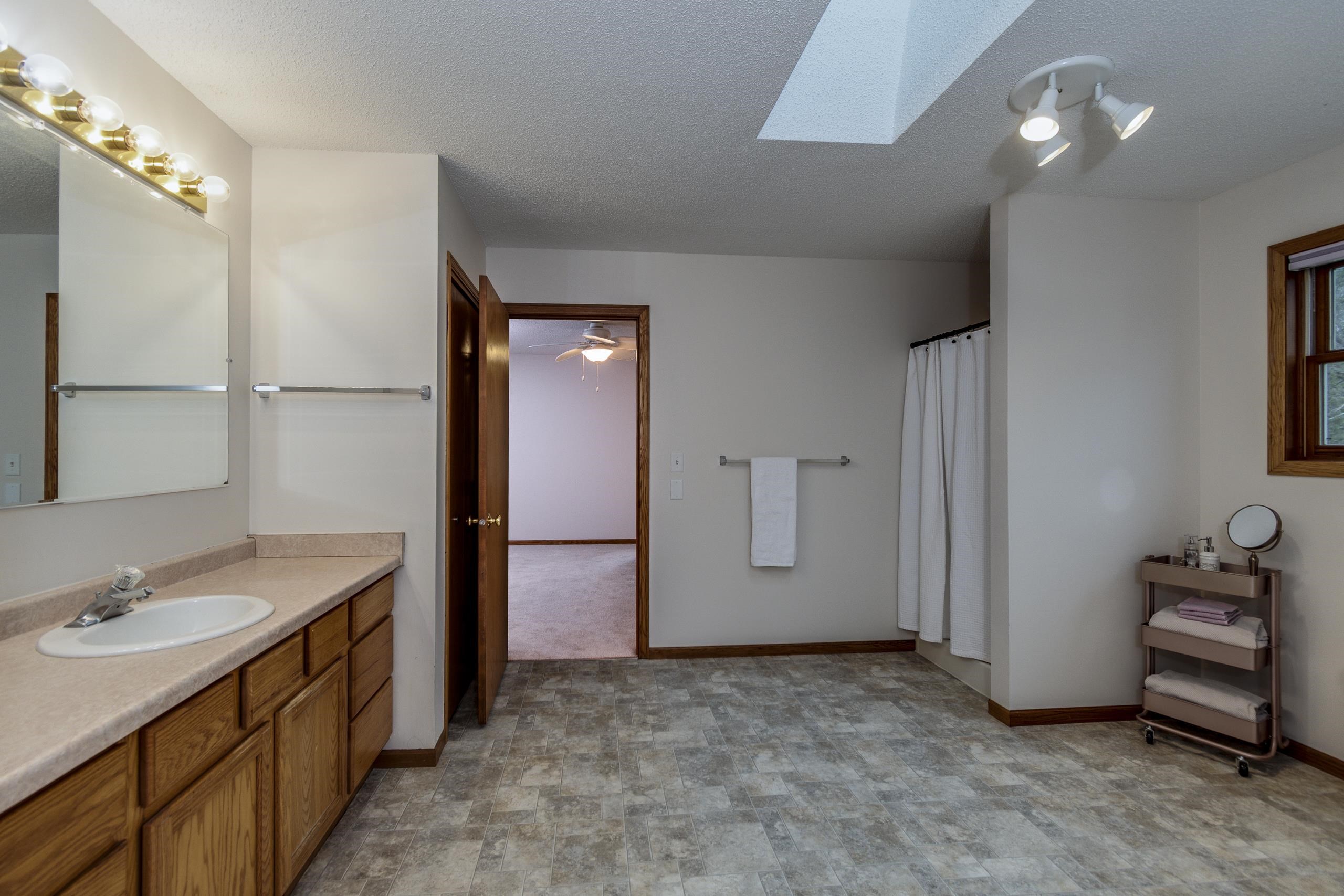 Spacious bathroom with a wood vanity, skylight, gray tile floor, and curtained shower.