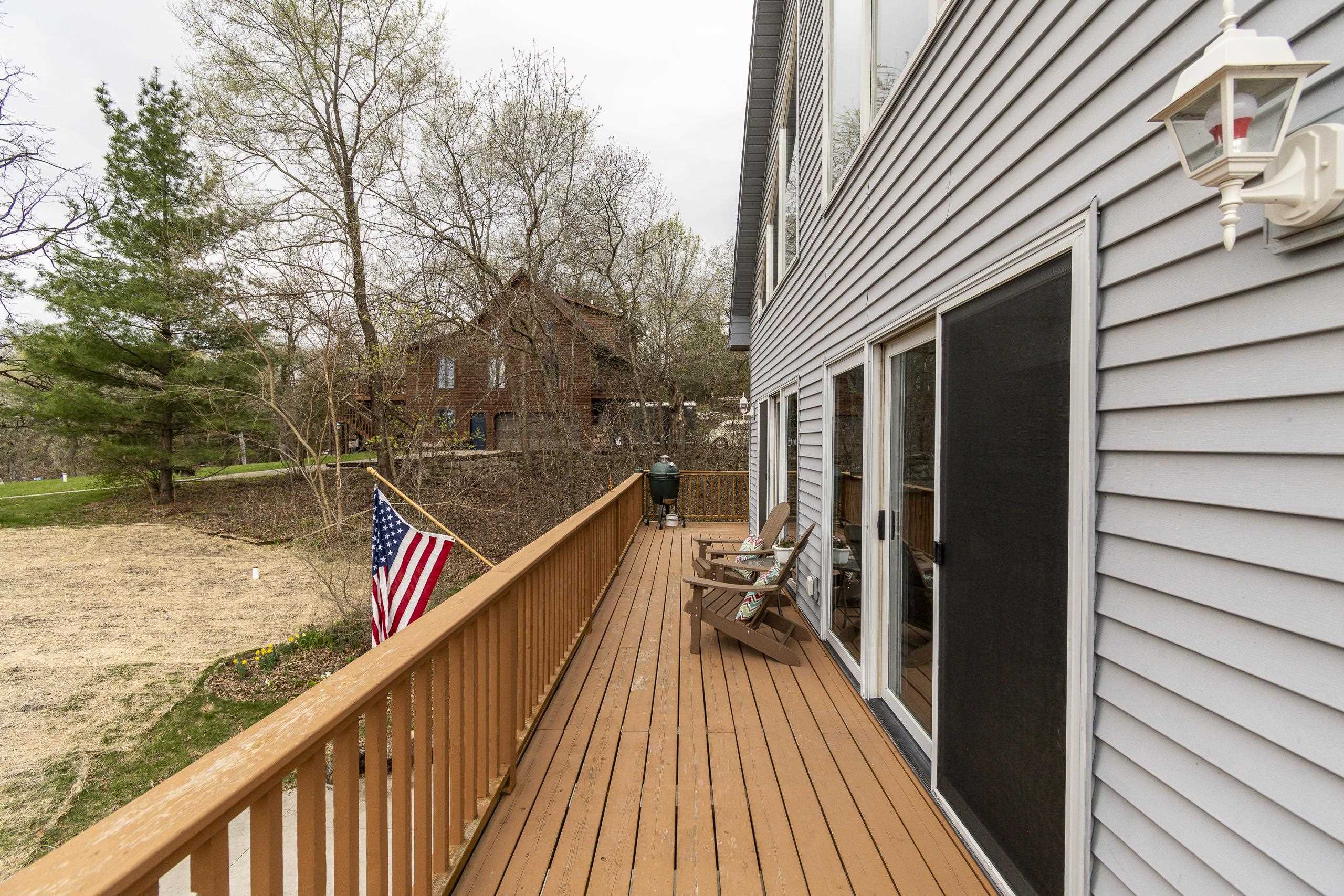 Wooden deck beside a gray-sided house, with Adirondack chairs, a grill, and an American flag.