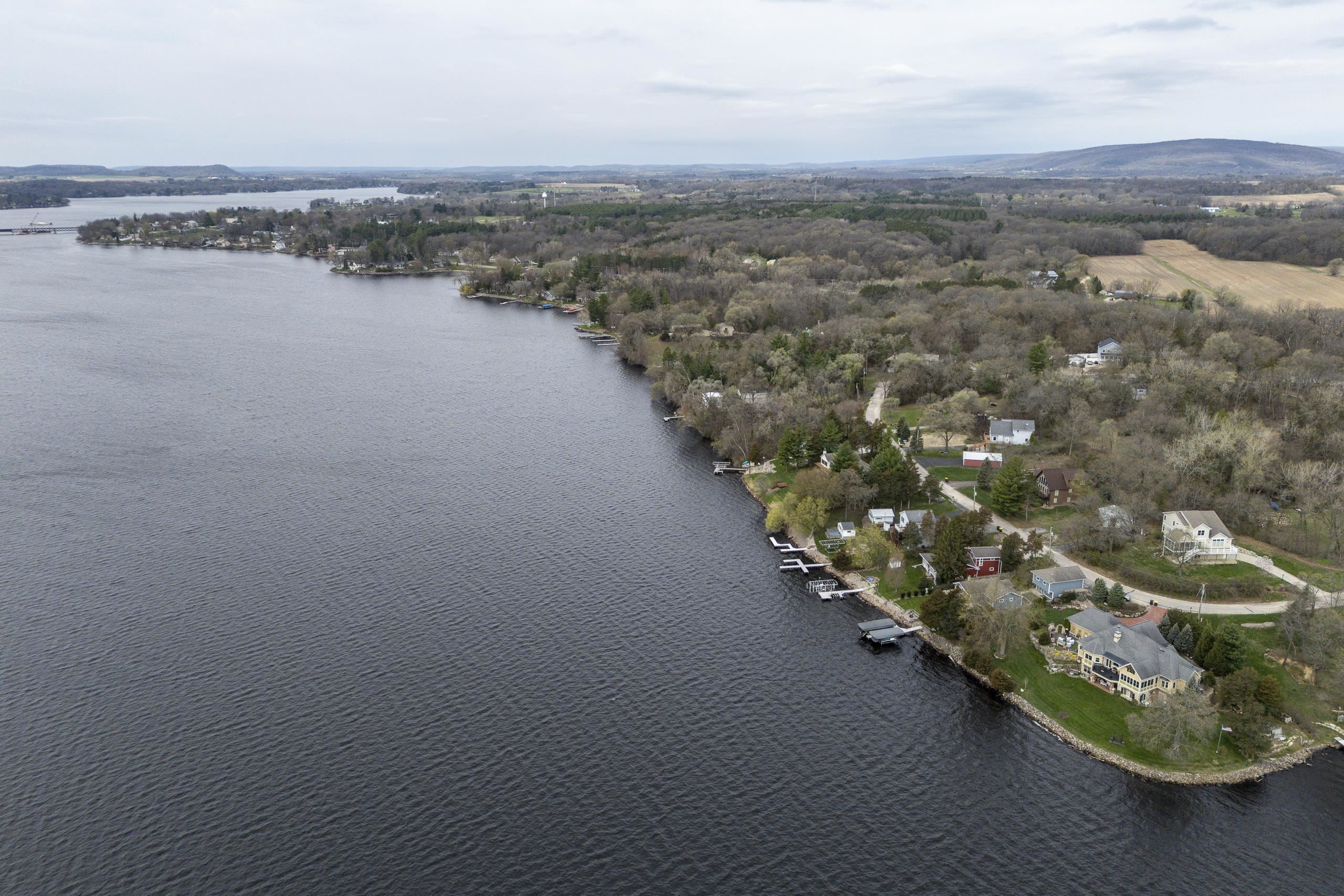 Aerial view of lakeside homes and docks along a wooded shoreline beside a broad lake.