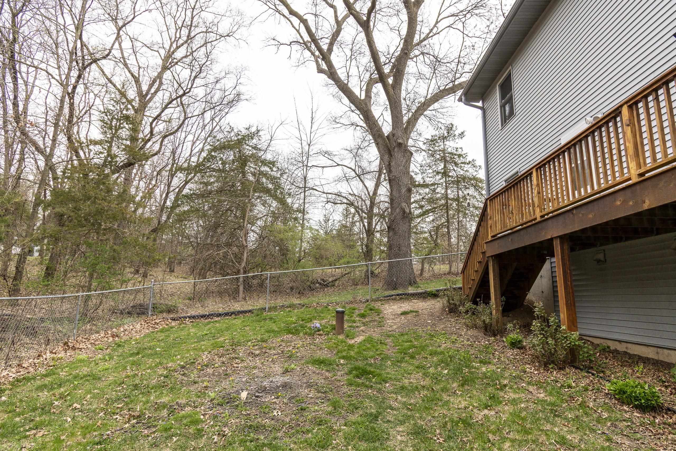 Backyard with a raised wooden deck, chain-link fence, and mature trees.