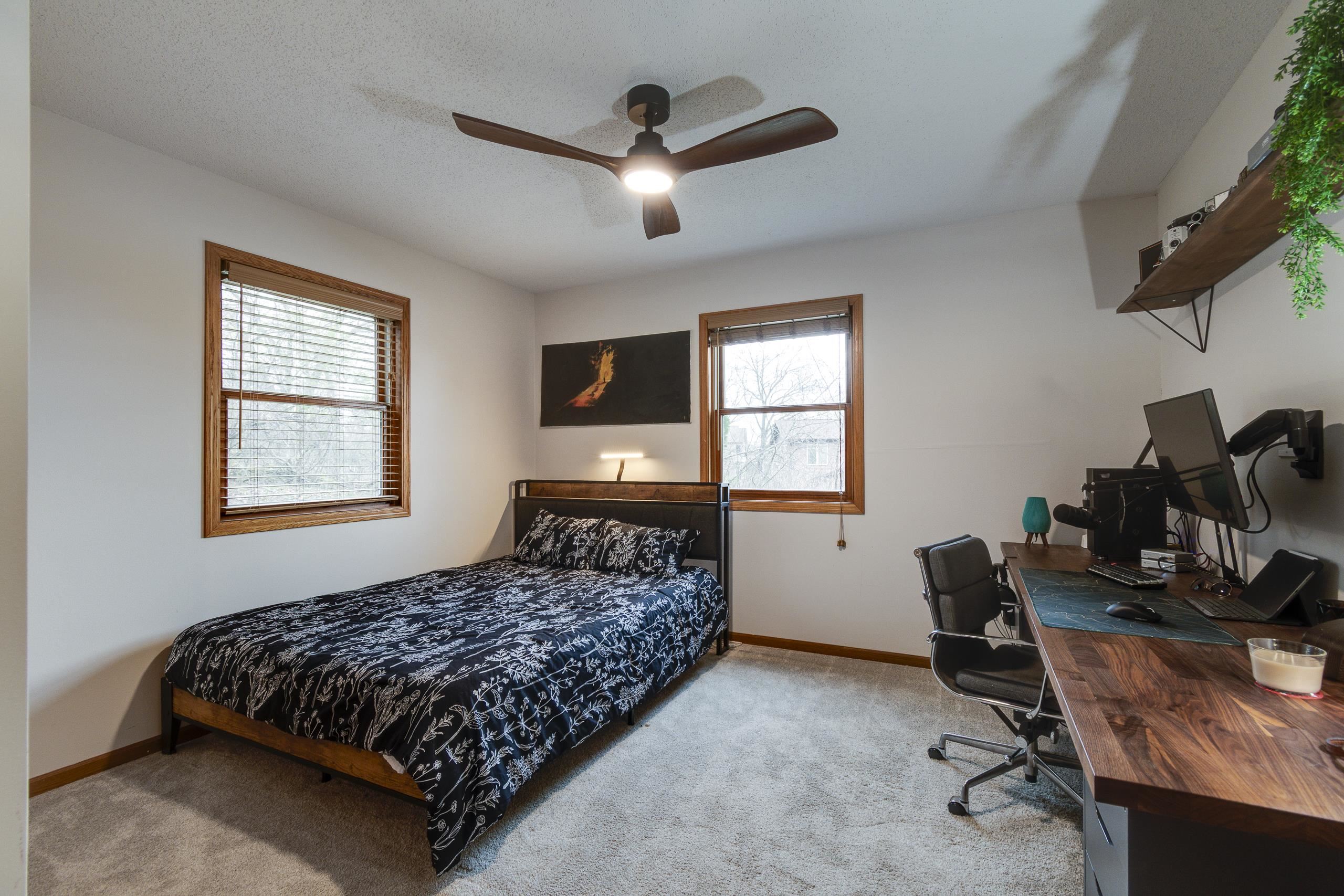 Bedroom with black floral bedding, wood-trimmed windows, and a computer desk.