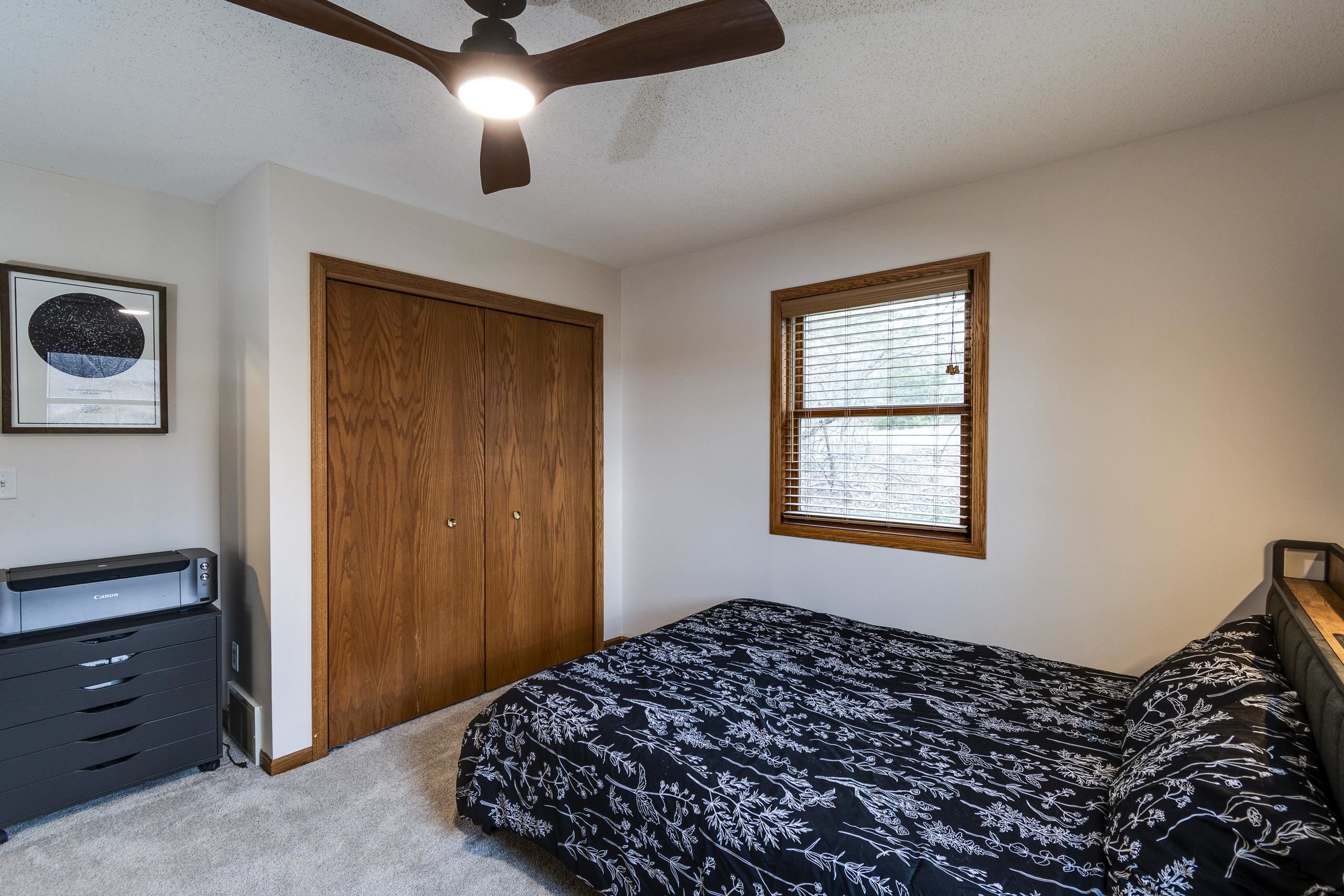 Bedroom with a black floral bedspread, wooden closet doors, and a window with blinds.