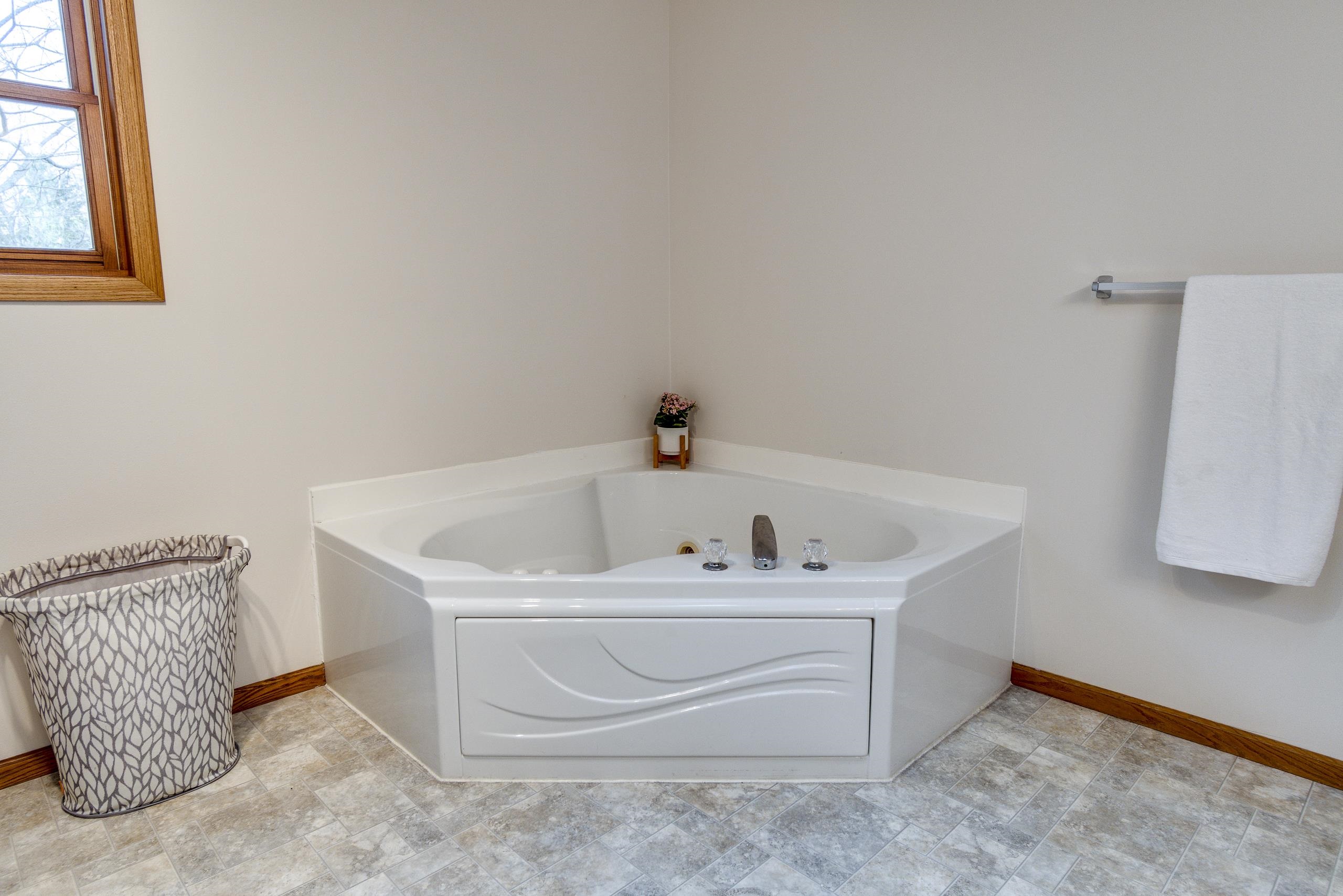 Bathroom with a large white corner jetted tub beneath a wood-trimmed window.