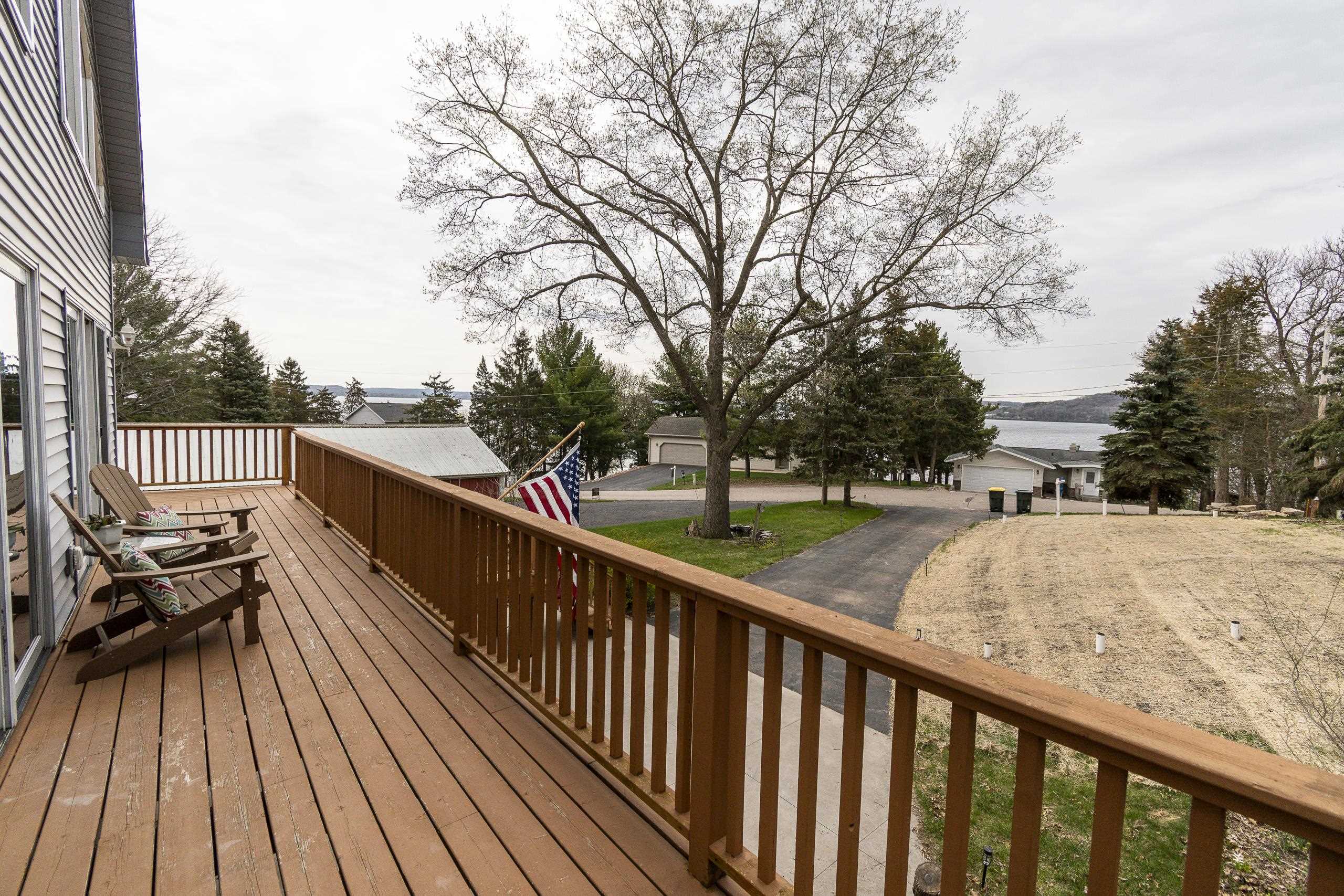Wooden deck with Adirondack chairs overlooking a lake and neighboring homes.