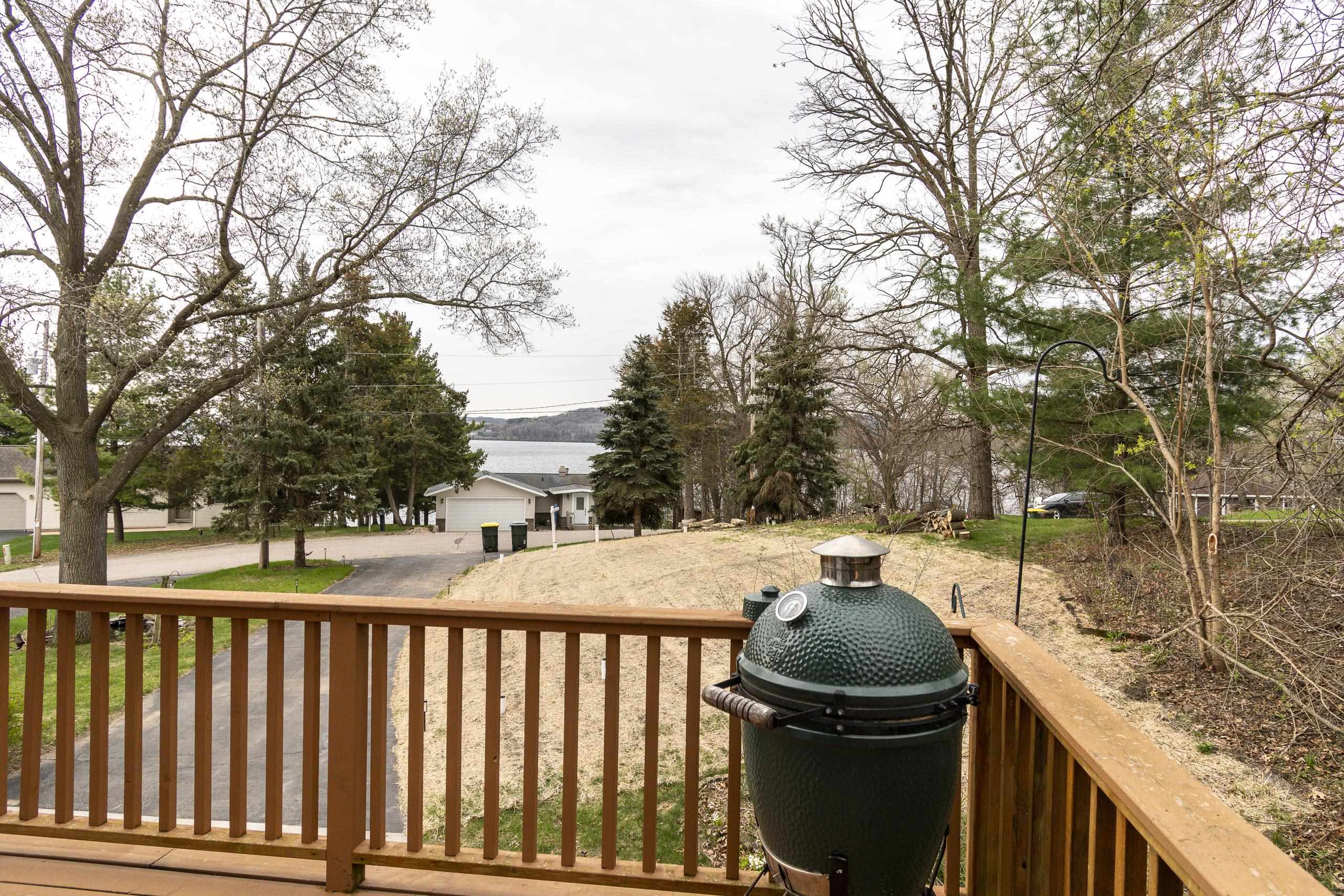 Wooden deck with a green ceramic grill overlooking a yard and lake.