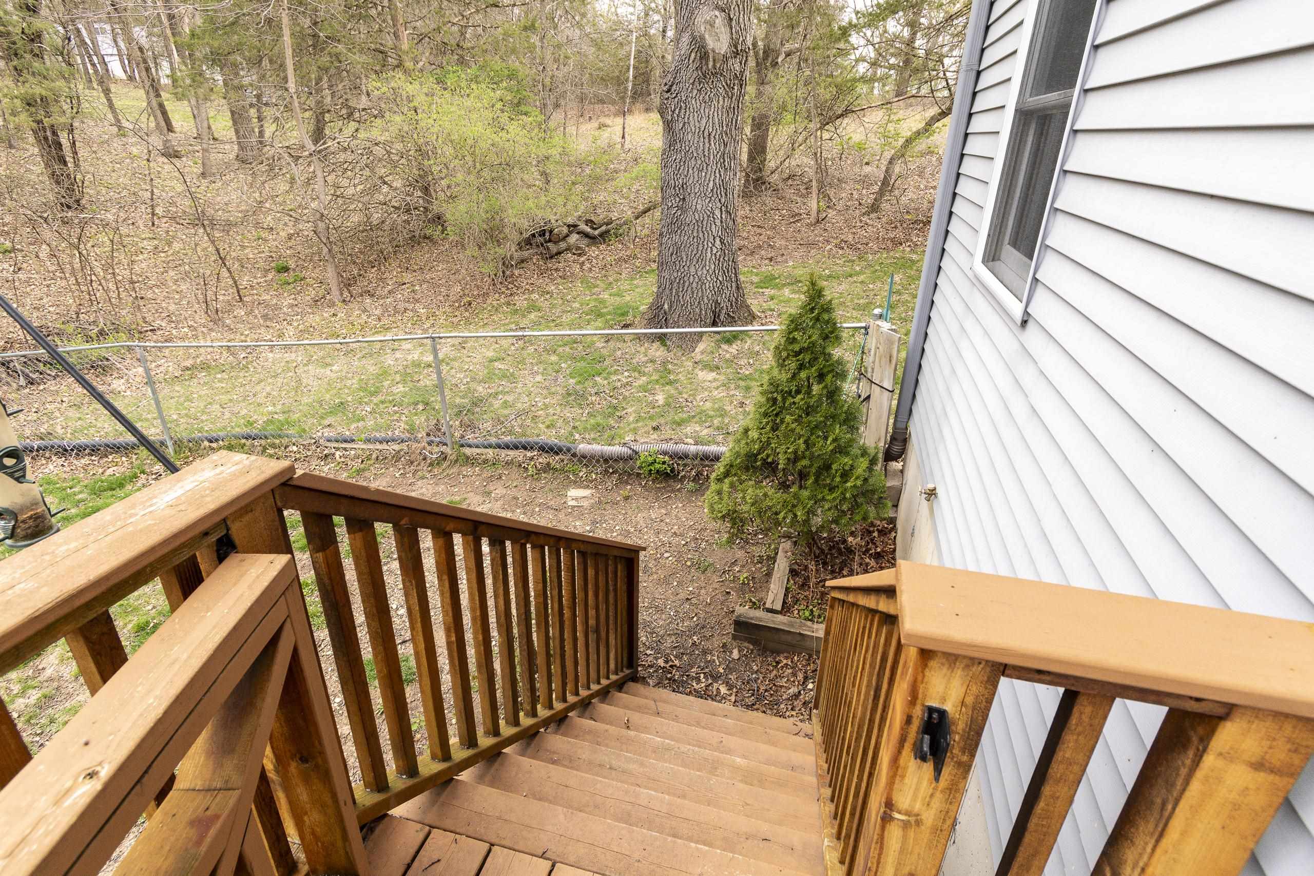 Wooden deck stairs lead down to a fenced, wooded backyard beside the house.