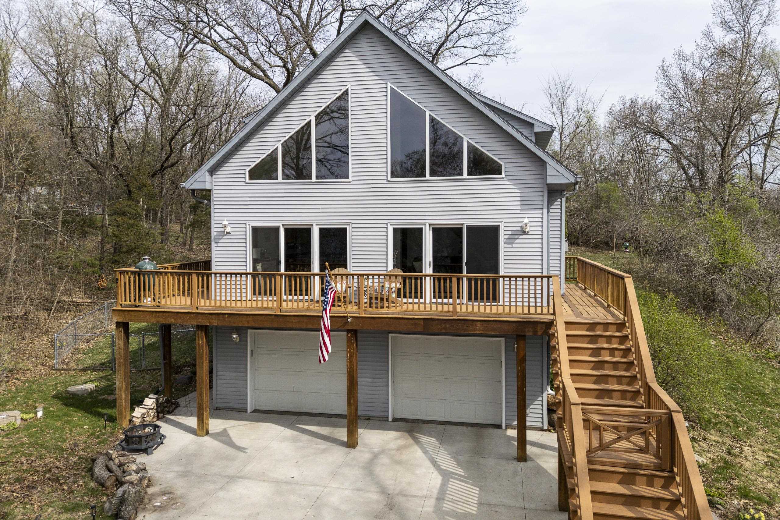 Gray gabled house with triangular windows, a raised wooden deck, and a long staircase beside the garage.