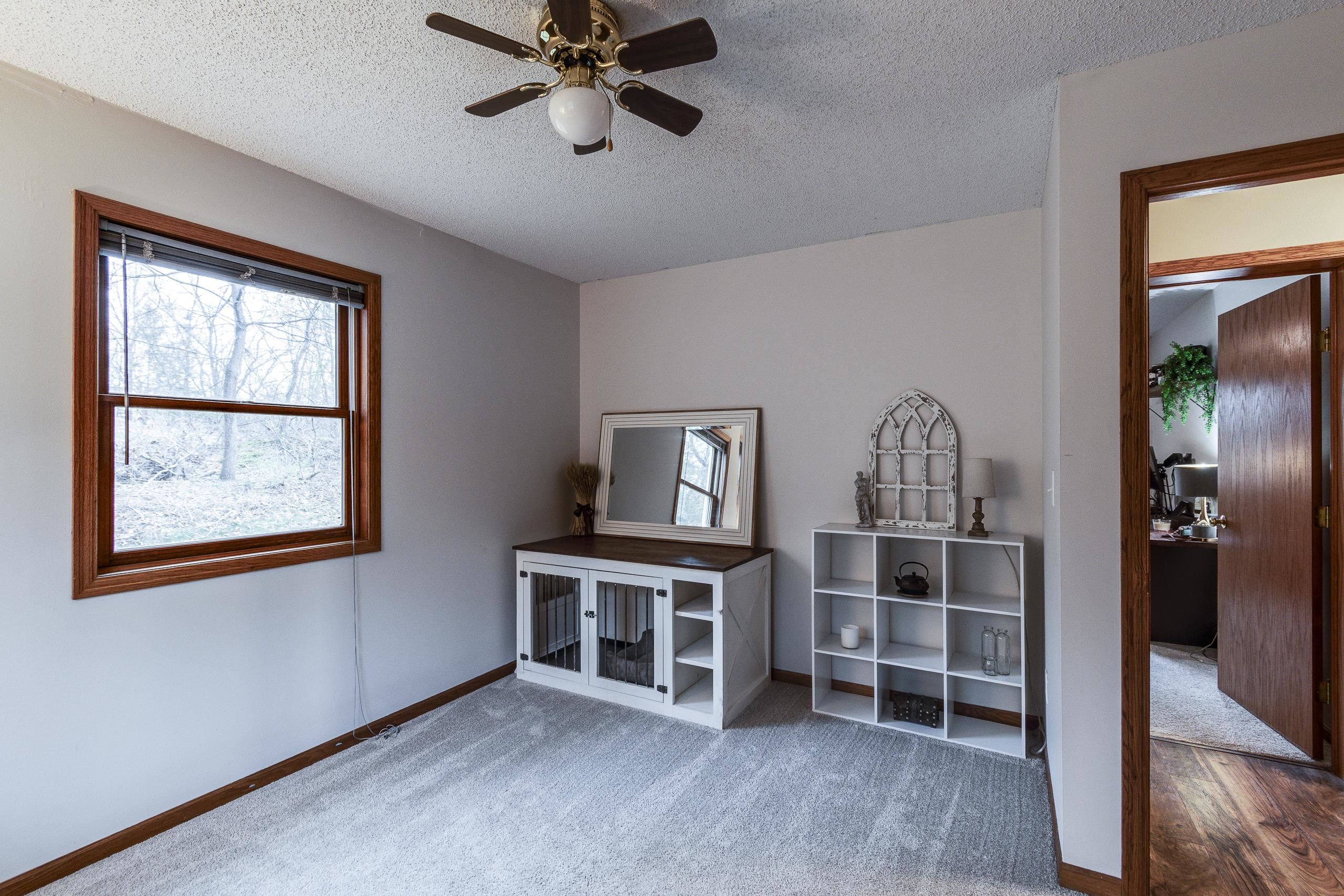 Carpeted room with a large window, ceiling fan, white shelving, and a pet crate cabinet.