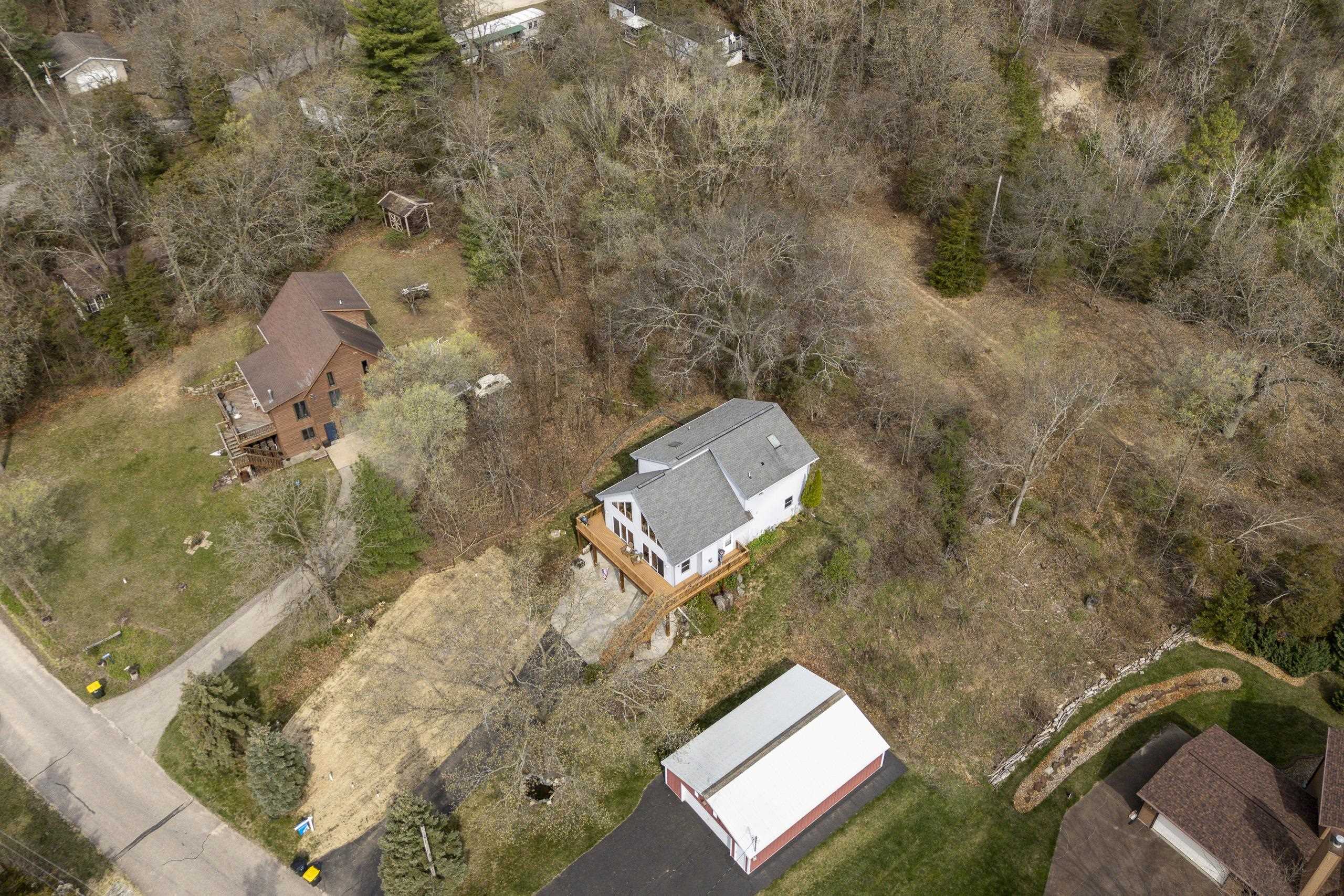 Aerial view of a white house with a raised deck, red outbuilding, and wooded lot.
