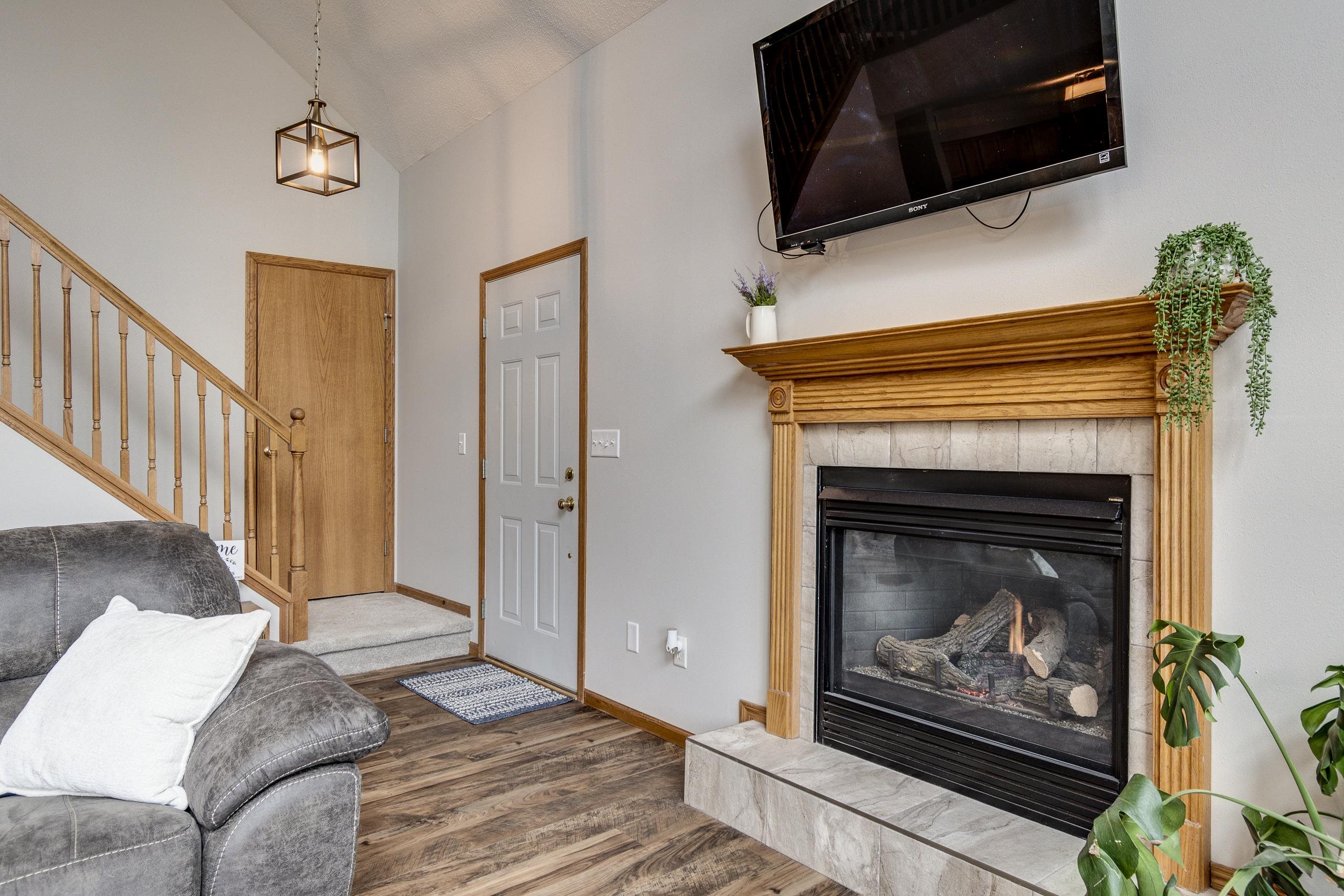 Living room with a stone fireplace, wood mantel, mounted television, and staircase.