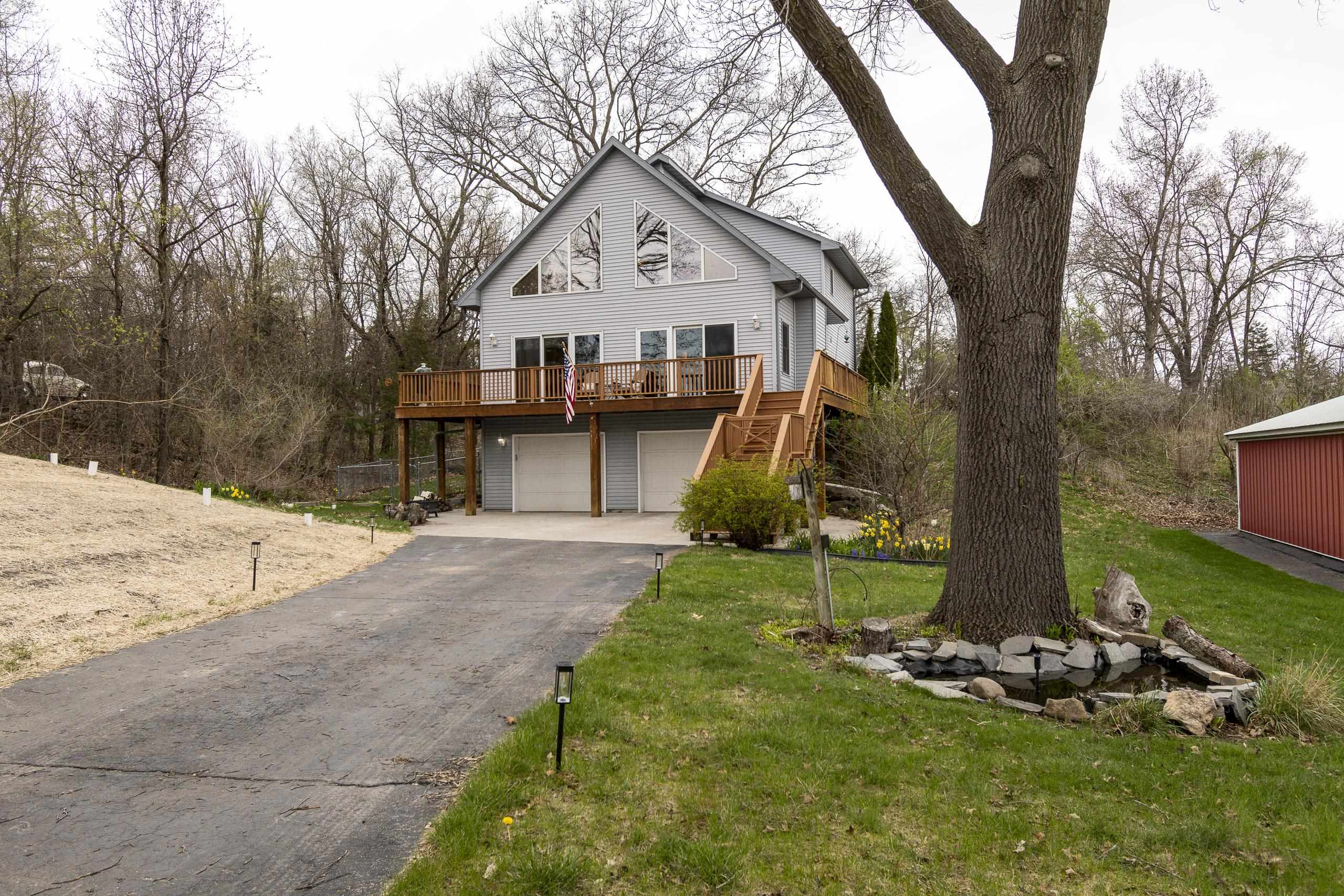 Gray gabled home with a raised wooden deck, two garage doors, and a wooded yard.