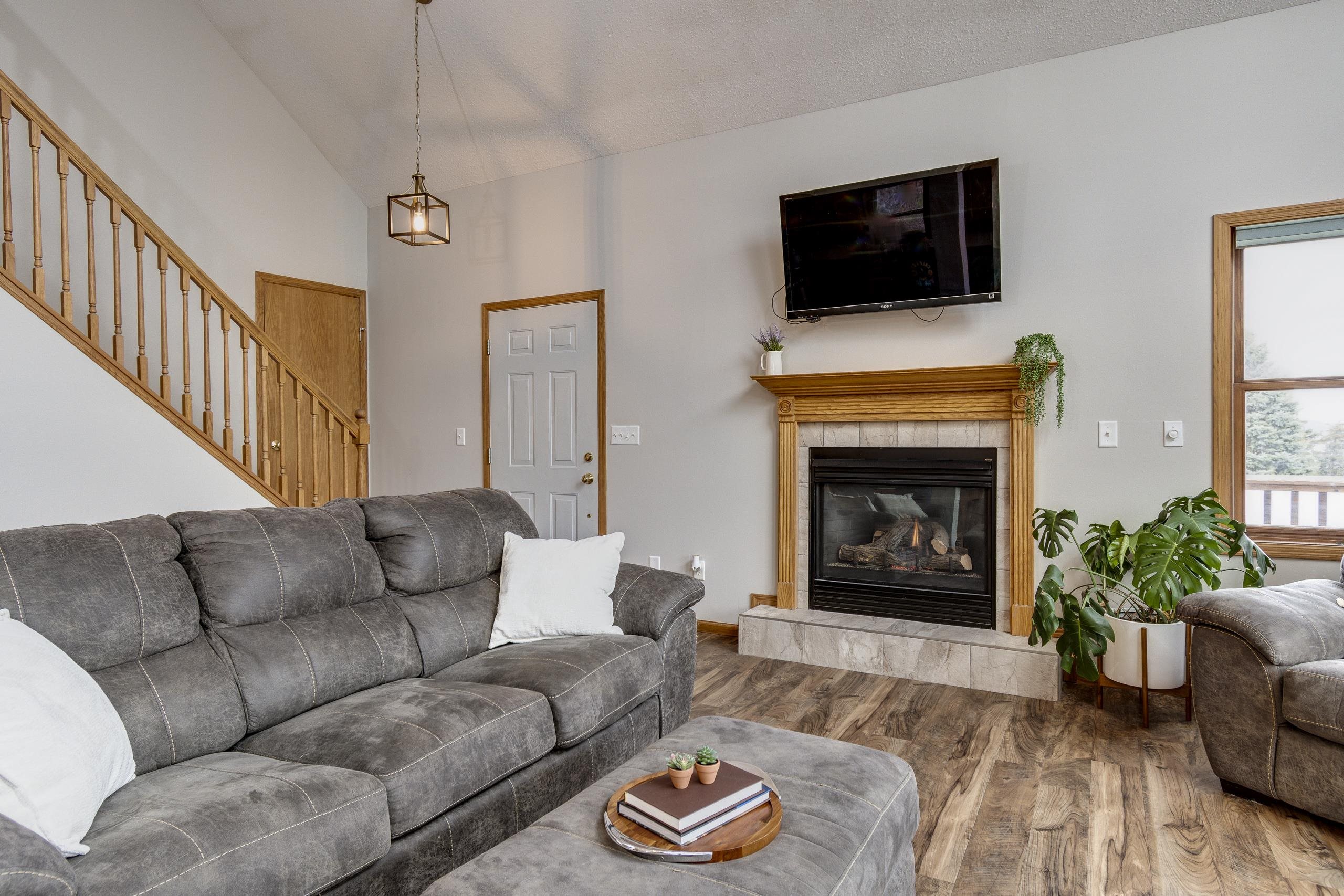Living room with a gray sectional, wood-trimmed fireplace, and staircase.