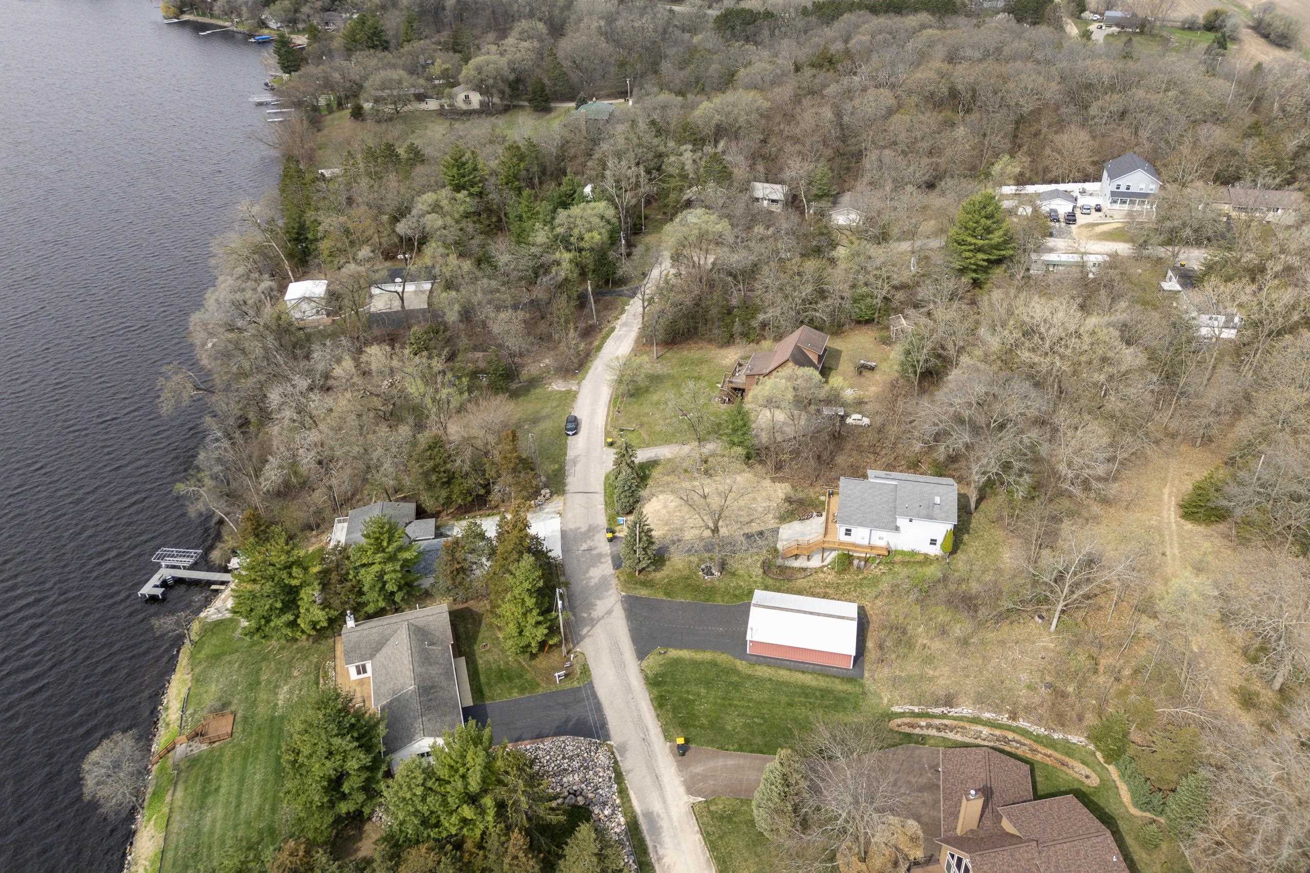 Aerial view of lakeside homes, wooded lots, docks, and a road beside the shoreline.