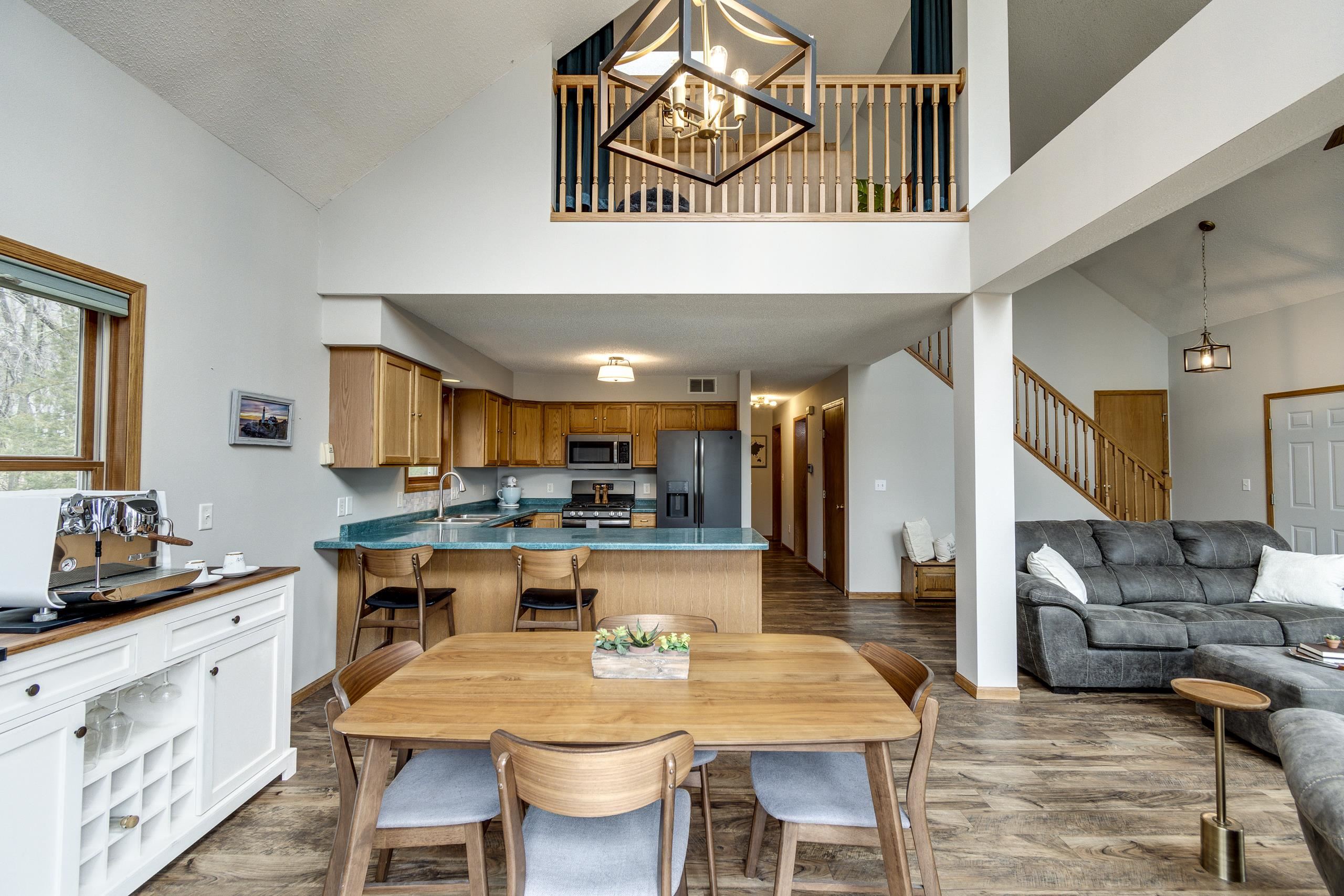 Open-plan kitchen, dining area, and living room with turquoise counters, wood cabinetry, and an upper-level railing.