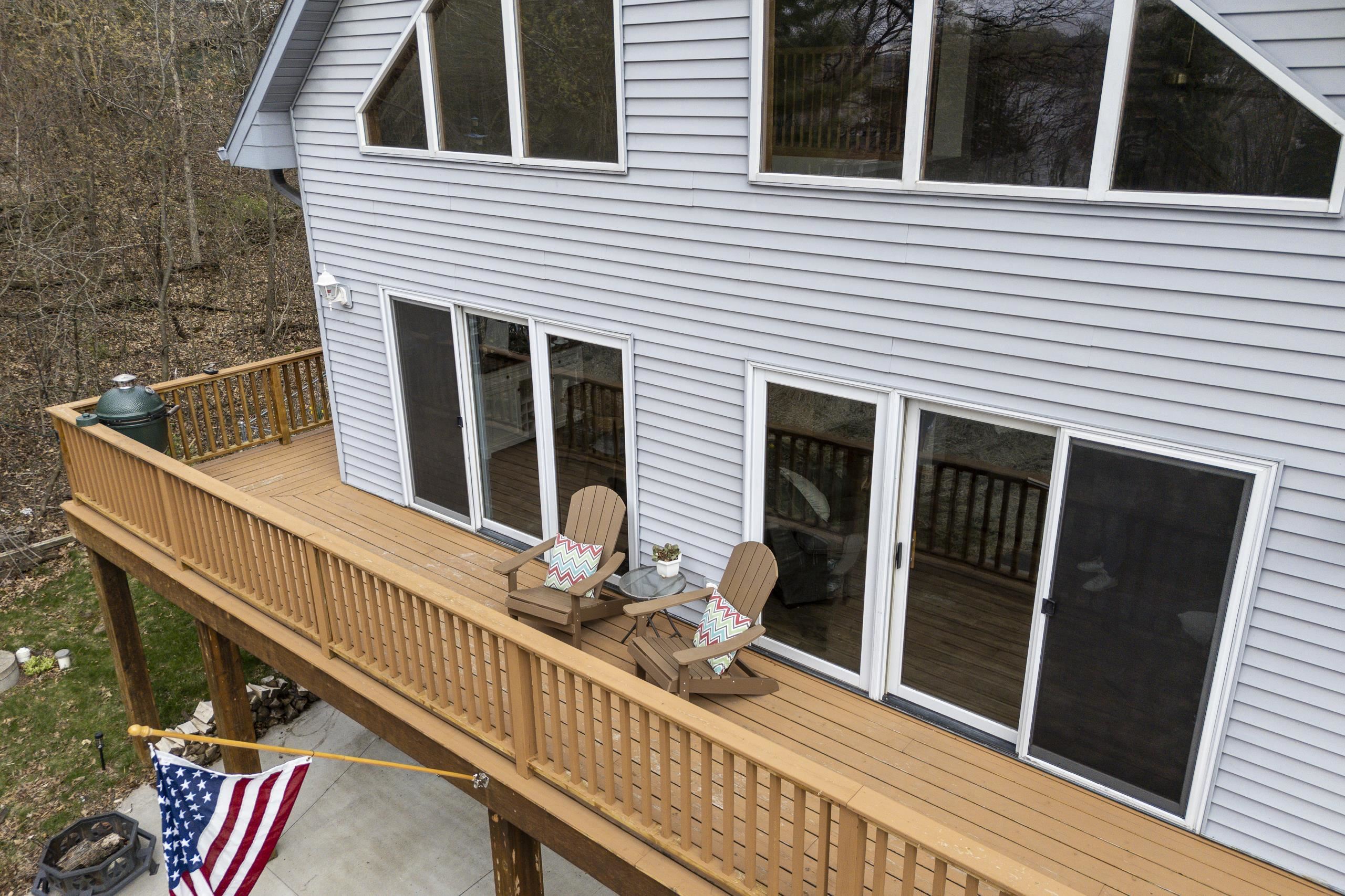 Wooden deck with two chairs along the gray-sided home, overlooking leafless woods.