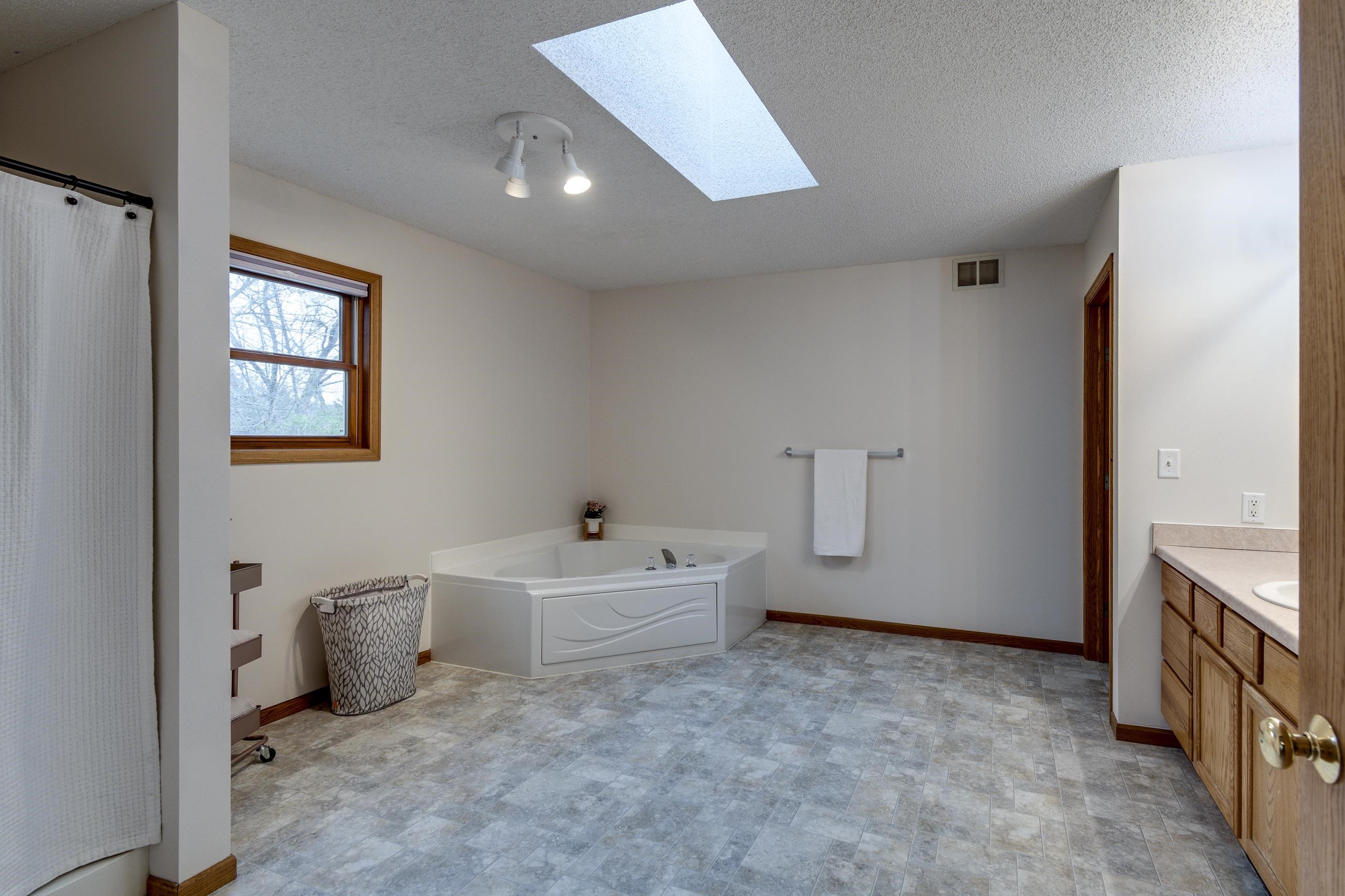 Spacious bathroom with a corner soaking tub beneath a skylight and a wood vanity.