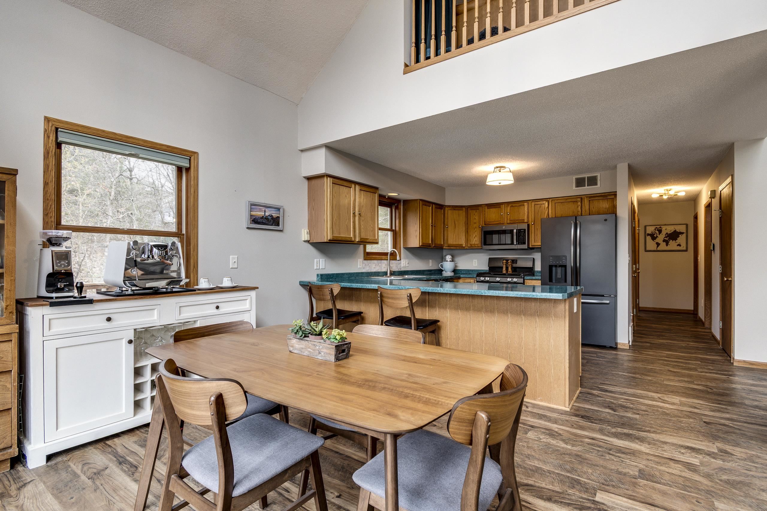 Open-plan kitchen and dining area with turquoise counters, wood cabinetry, and a loft railing.
