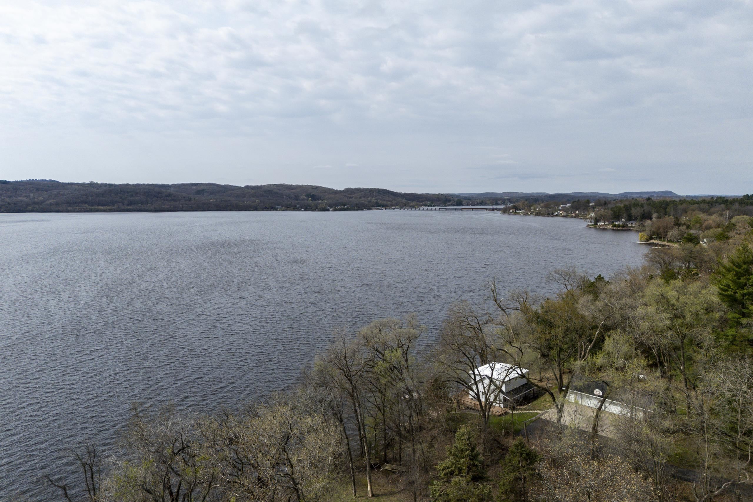 Aerial view of a wooded lakeshore home beside a broad lake, with distant hills and homes across the water.