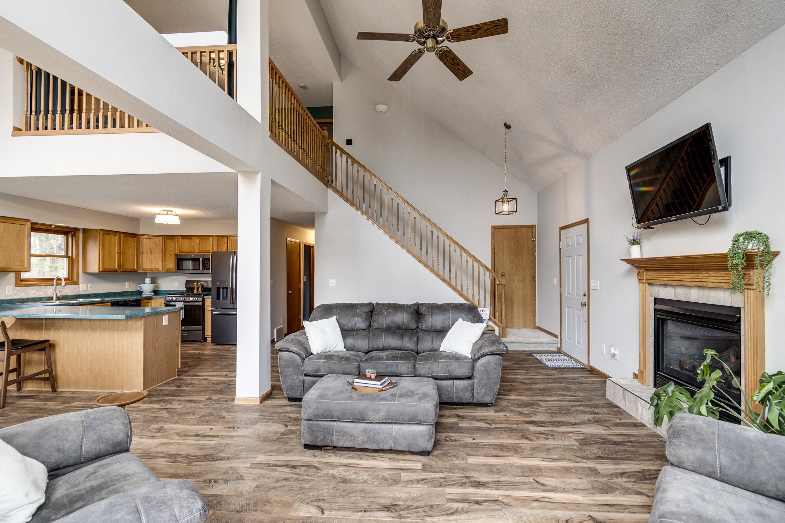 Living room with vaulted ceiling, open staircase, gray sofa, and wood-mantel fireplace.