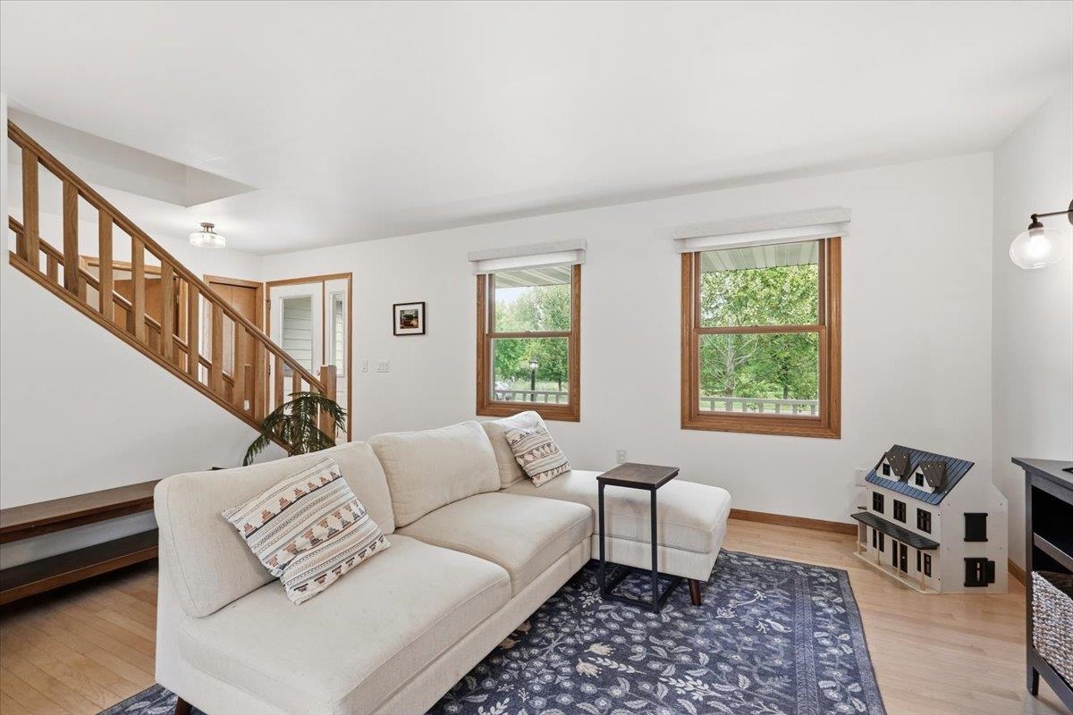 Living room with a white sectional, patterned rug, wood staircase, and windows overlooking greenery.
