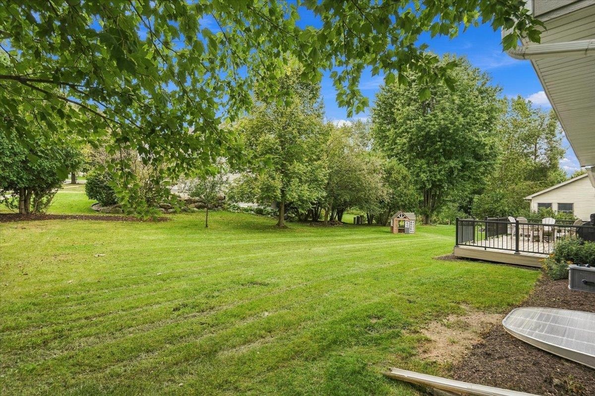 Spacious backyard lawn bordered by mature trees, with a small playhouse and raised deck.