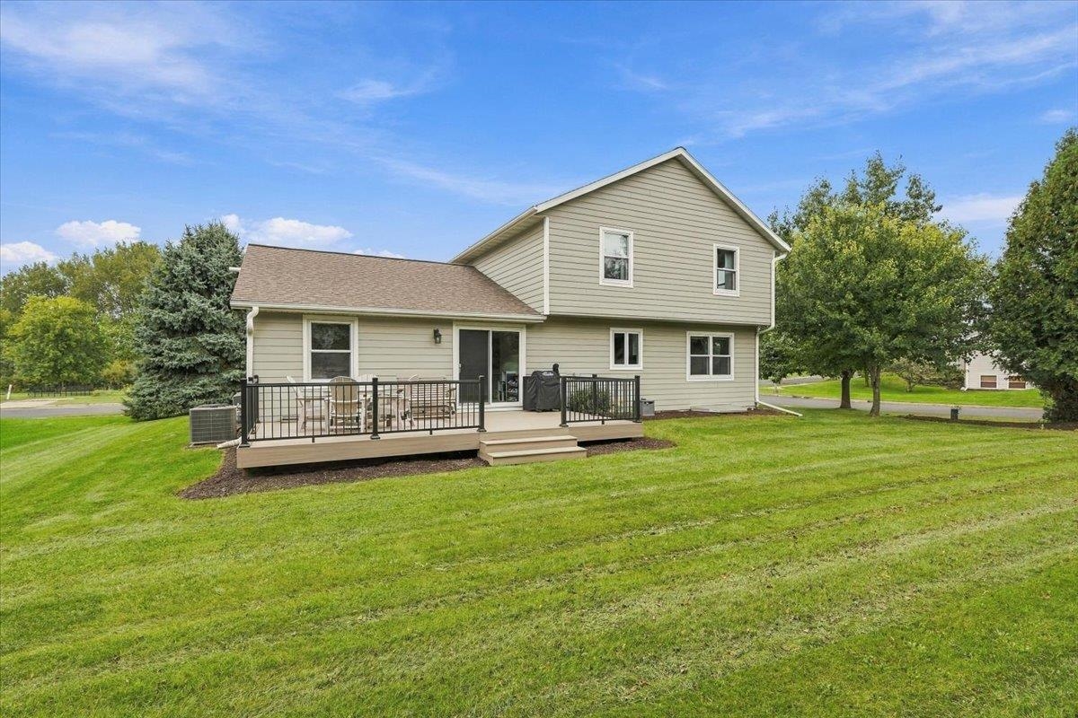 Two-story home with a raised deck and patio furniture overlooking a broad green lawn.