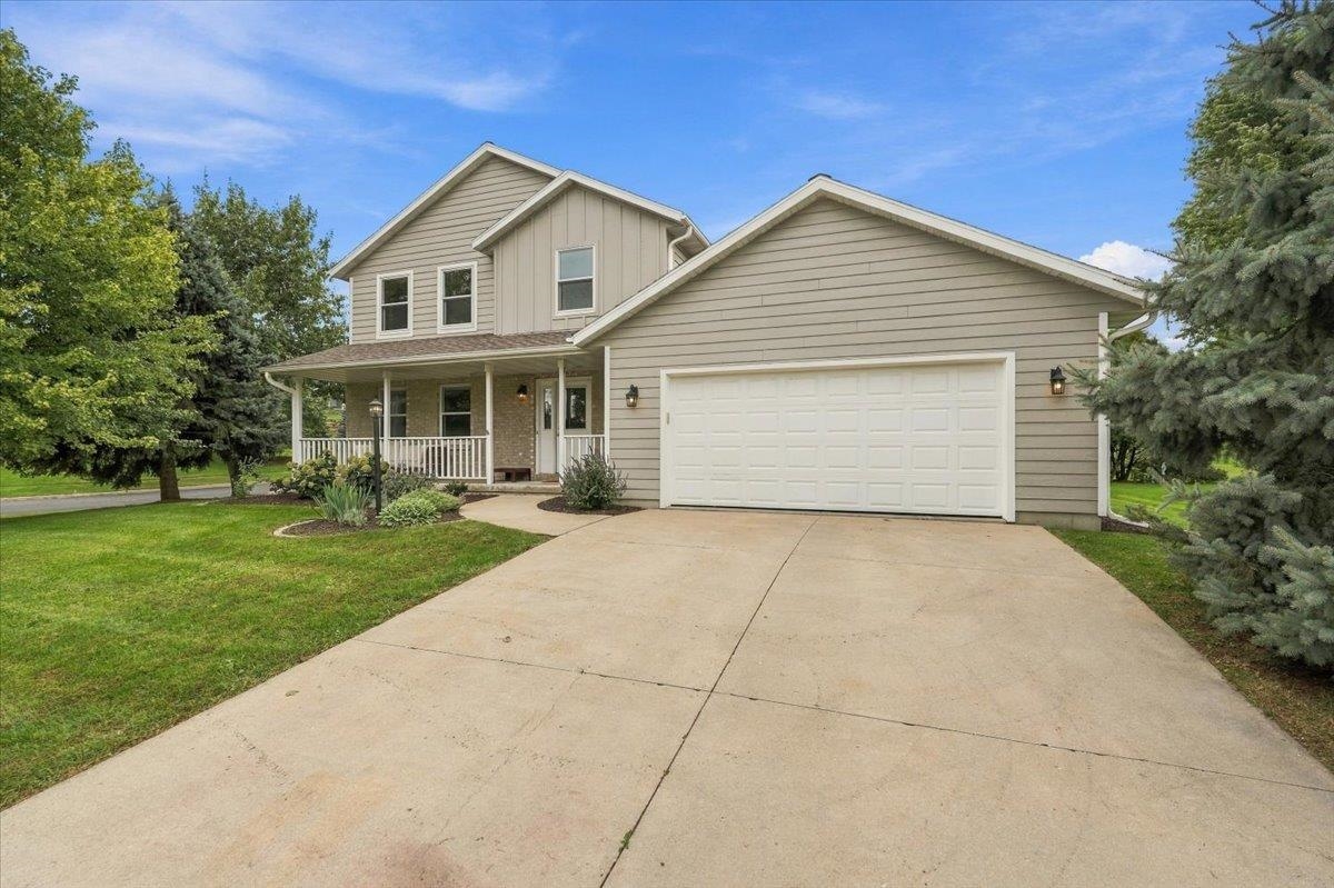 Two-story beige home with a covered porch, double garage, and broad driveway.