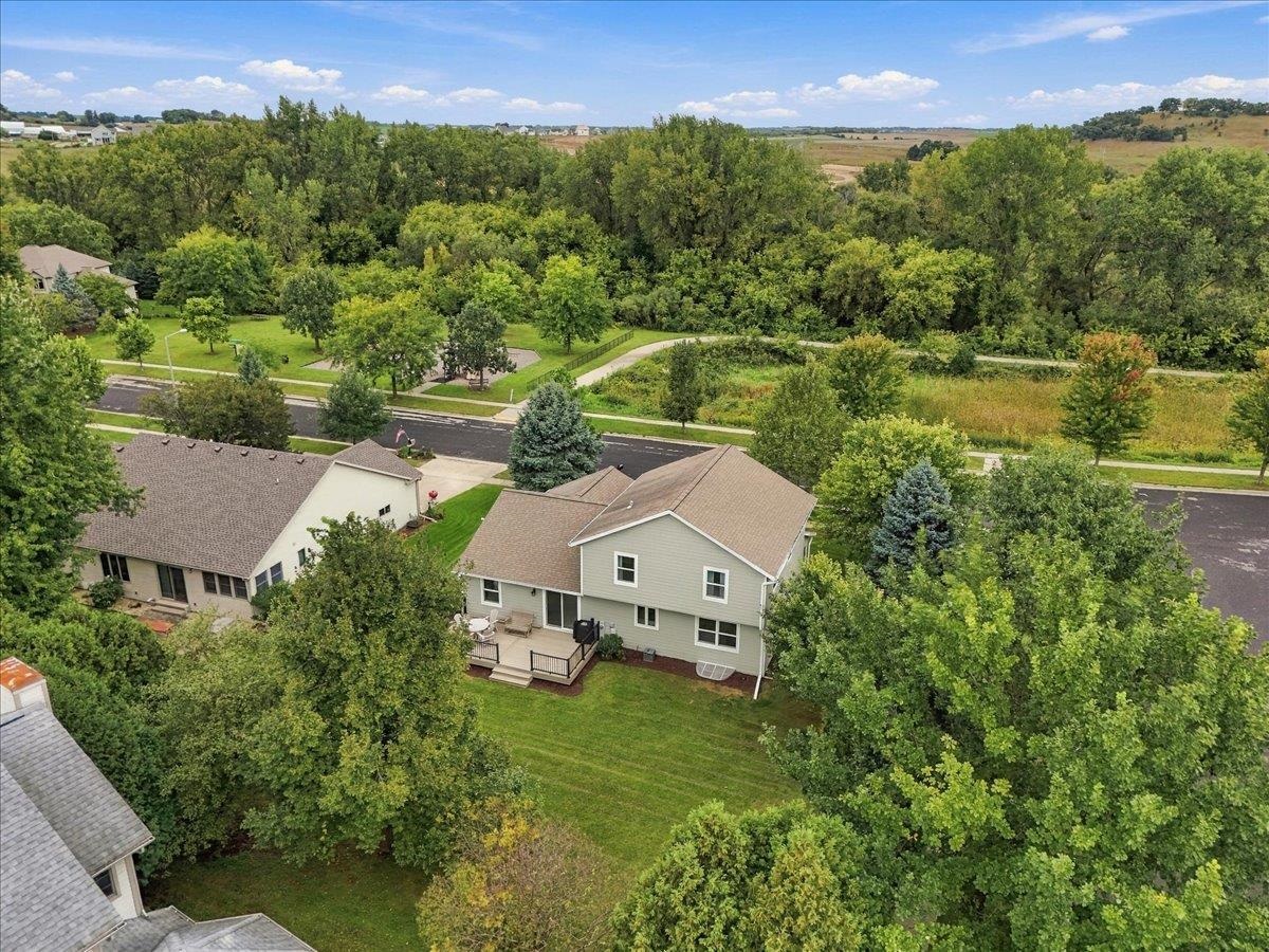 Aerial view of a two-story home with a deck and leafy backyard beside wooded parkland.