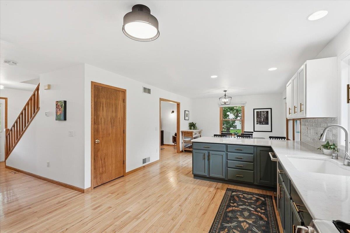Open kitchen with a dark blue island, white counters, and light wood floors beside a wood-railed staircase.