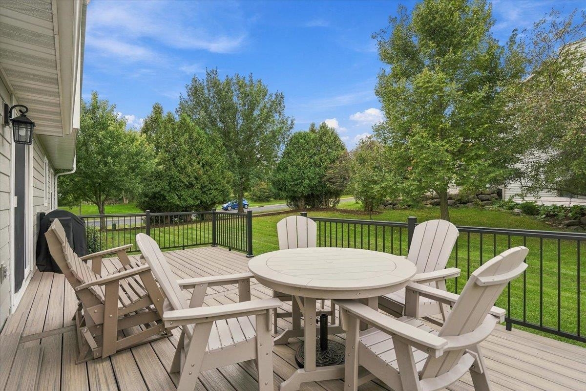 Furnished backyard deck with white Adirondack chairs overlooking a tree-lined lawn.