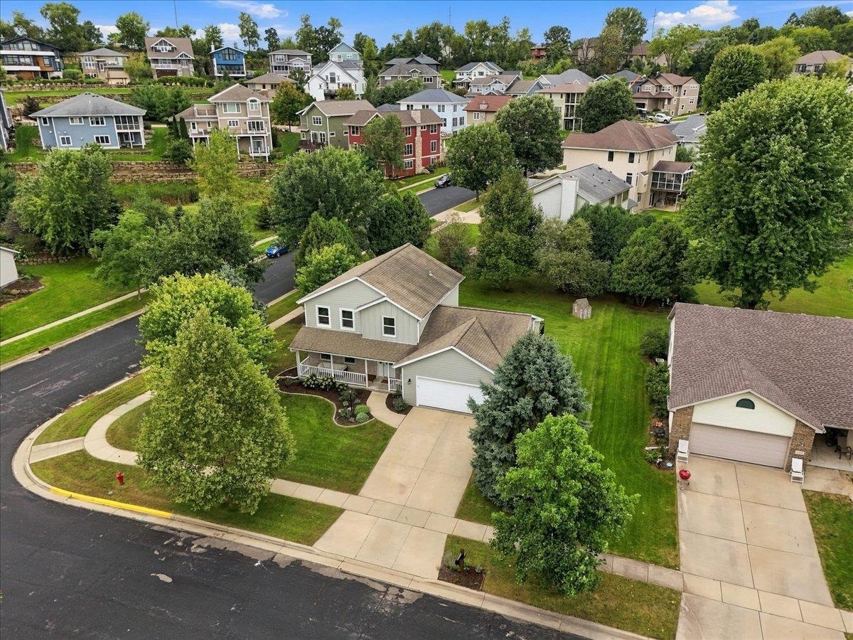 Aerial view of a gray two-story home with an attached garage and landscaped yard in a leafy neighborhood.
