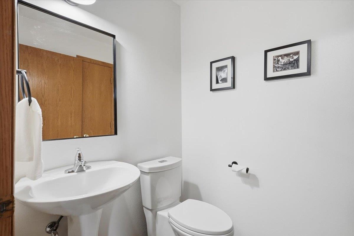 Bathroom with a pedestal sink, toilet, large mirror, and framed wall art.