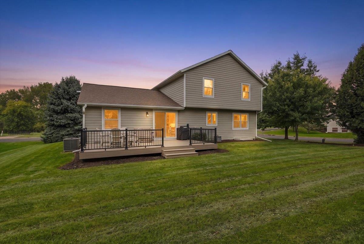 Two-story gray house with a raised deck and black railings at dusk.