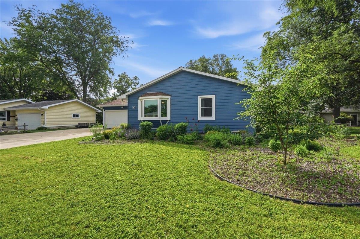 Blue single-story home with a bay window, landscaped garden beds, and a broad front lawn.